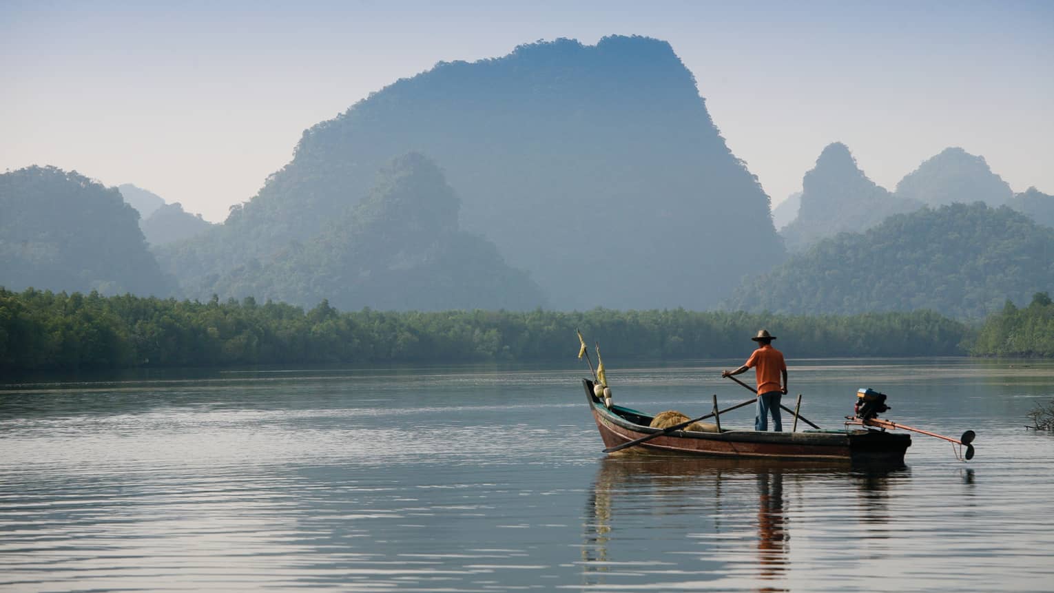 Man in a boat on Langkawi river with mountains in the background