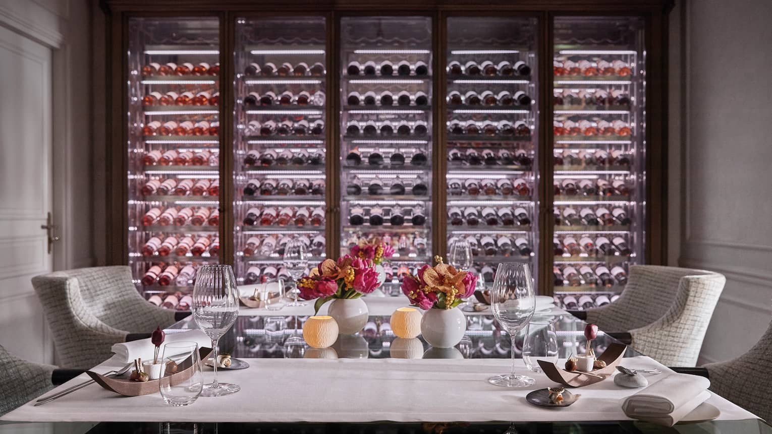 A private dining room with two chairs and an illuminated wall of wine on display