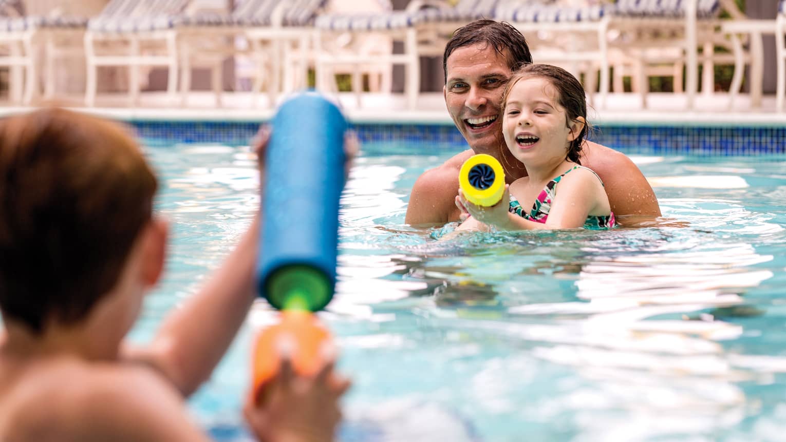 Smiling family swimming in outdoor pool squirt water guns at each other