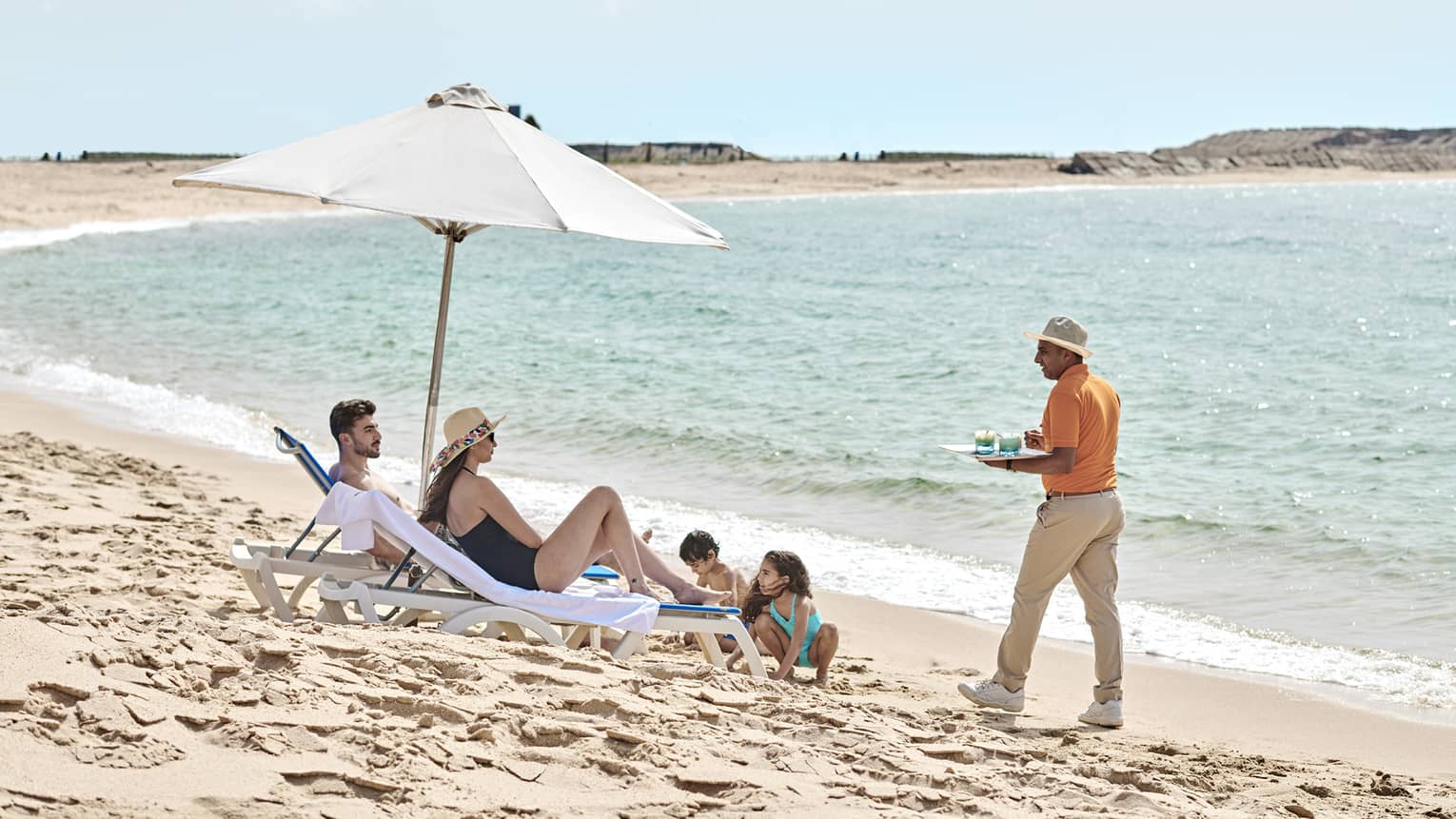 a family lounges on the beach in alexandria while a four seasons staff serves them refreshments