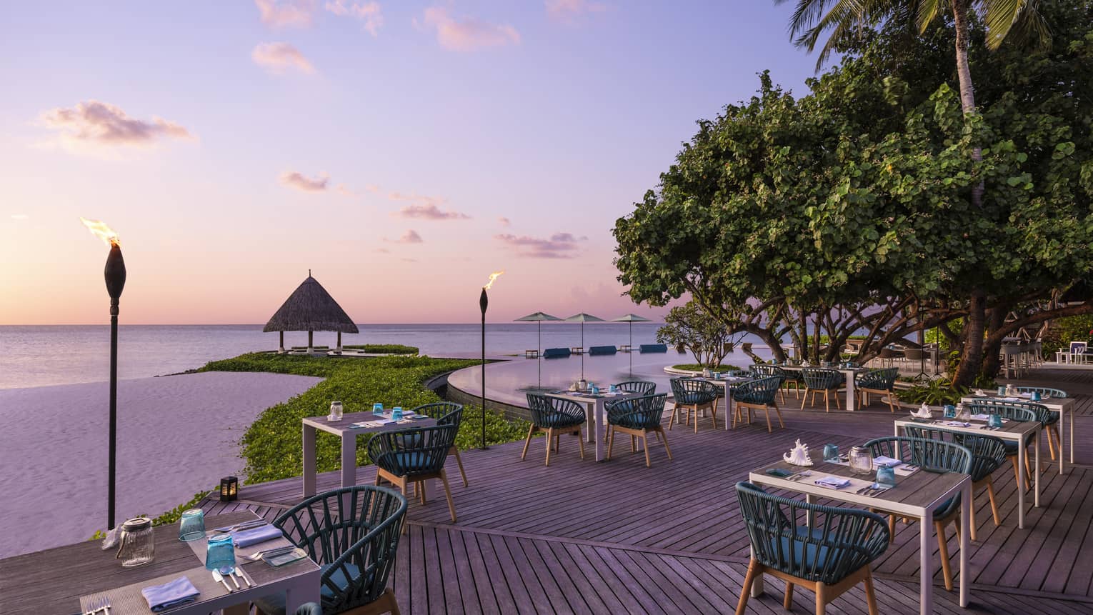 Tiki torches line the oceanside Reef Club terrace that's ready for guests with tables set with plates, silverware, blue napkins, all overlooking the ocean