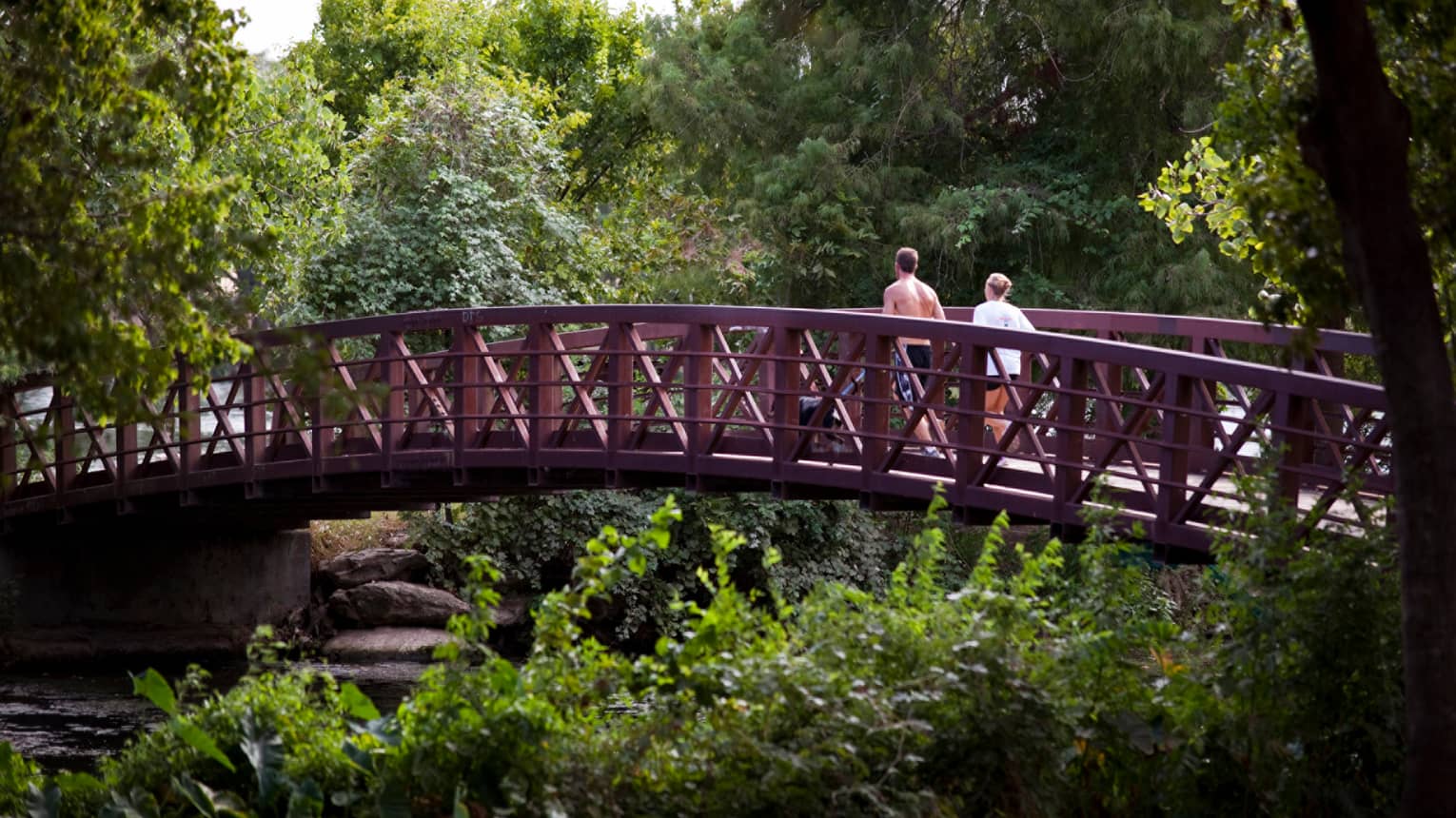 Two people jog across wood bridge surrounded by trees, forest