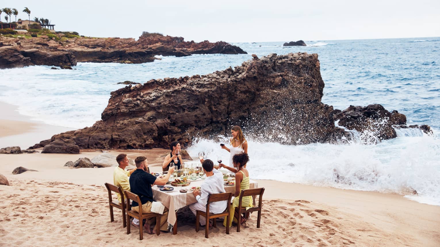 A group eating at a table on a beach with waves crashing nearby.