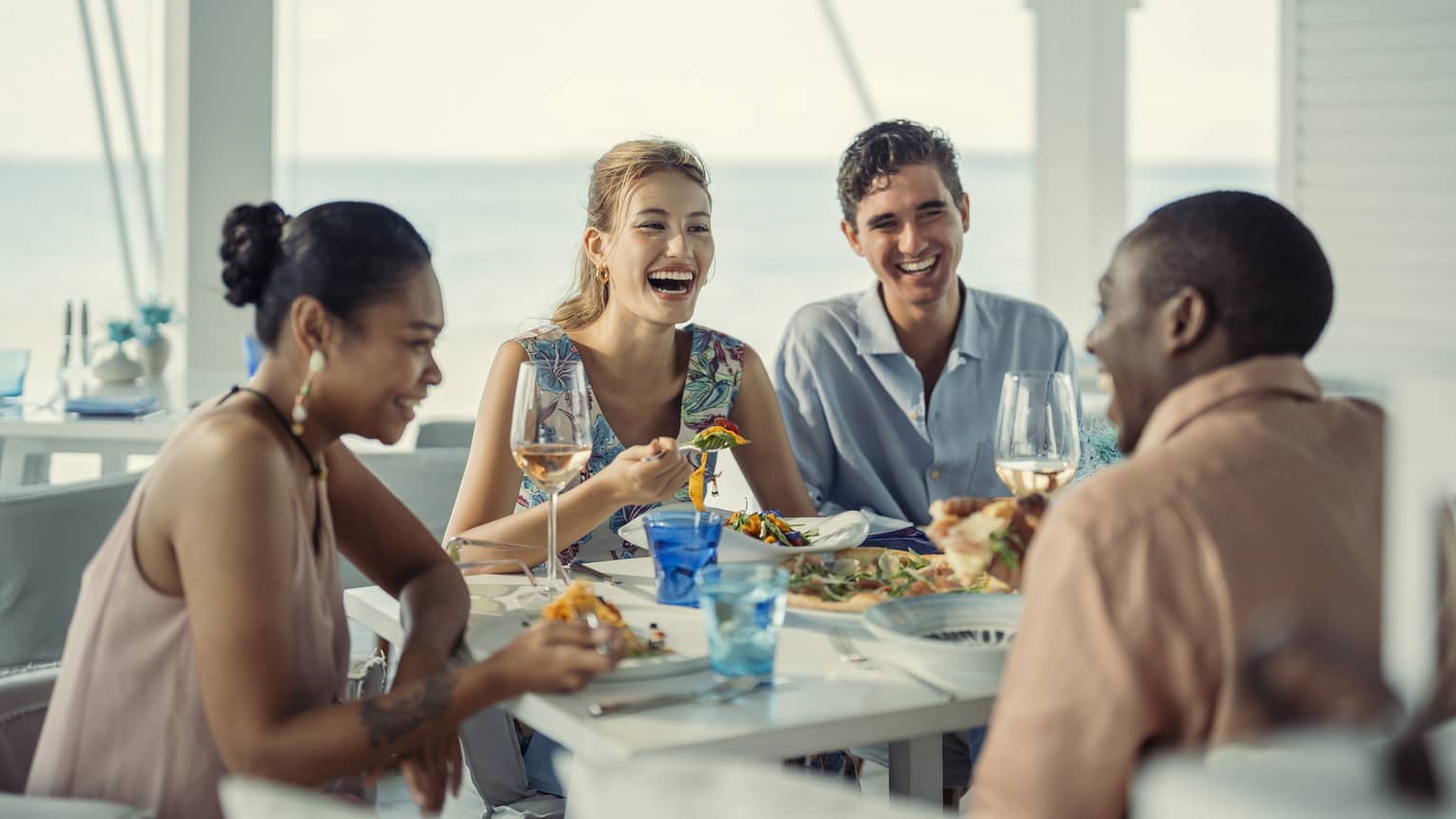 Two couples laugh over a meal at Blu Beach Club