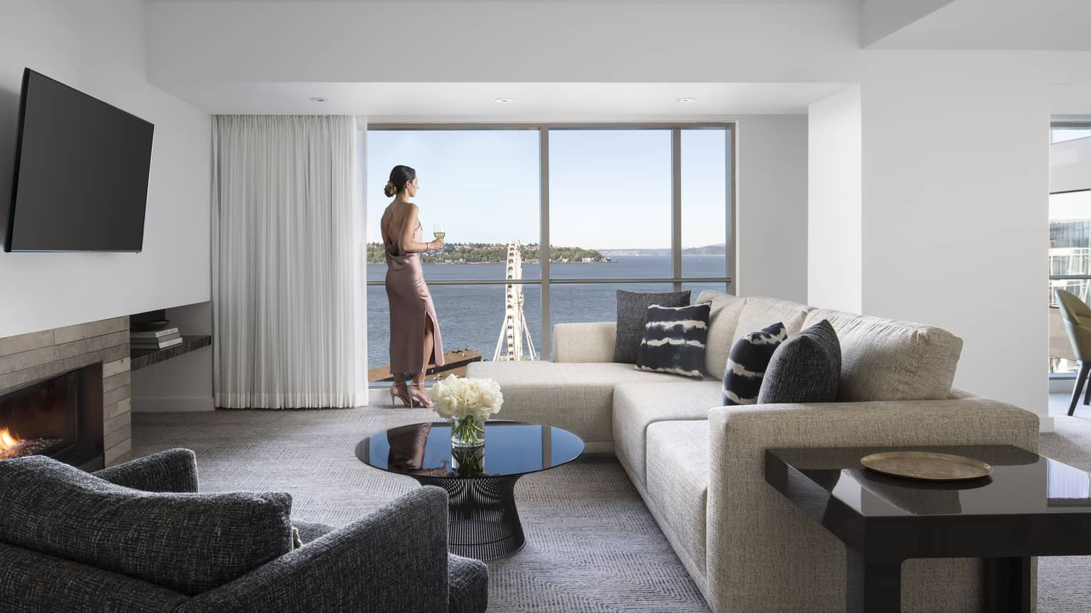 Woman stands at sunny window near L-shaped sofa in Deluxe Elliot Bay Suite 
