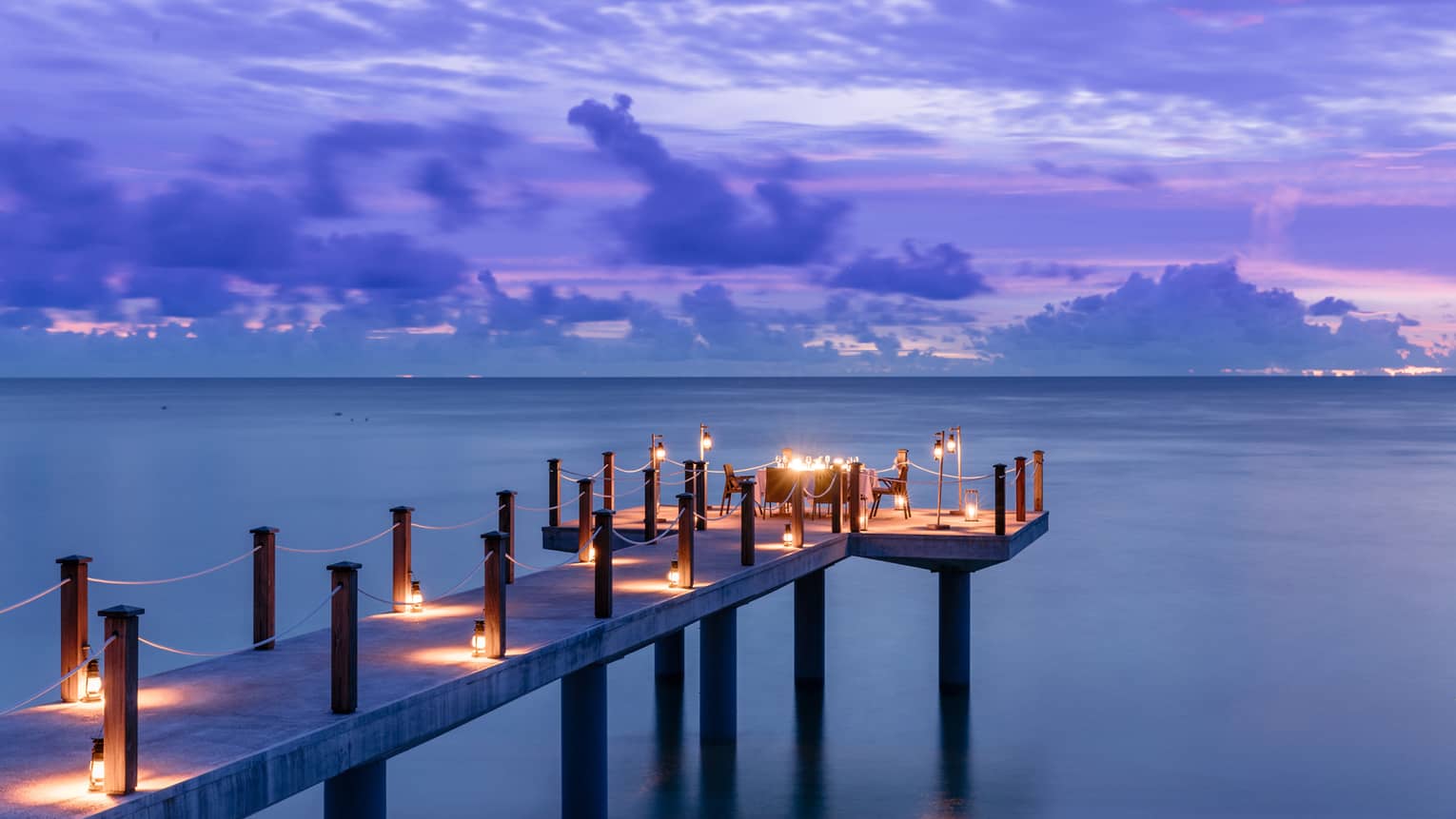 Candlelit jetty off Desroches Island with purple sunset hues