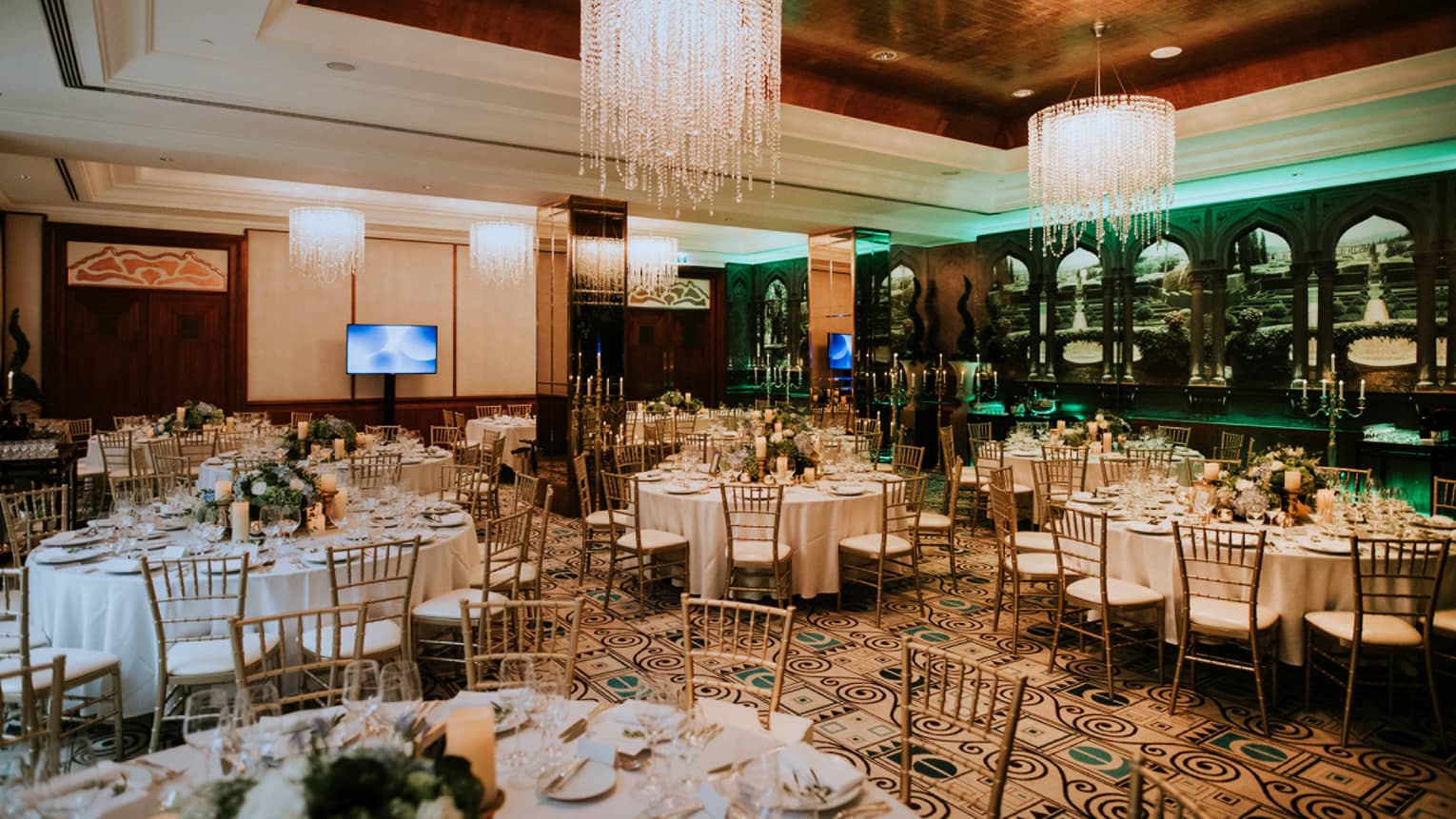 Round dining tables and chairs, flowers and candles in room with high ceilings and chandeliers