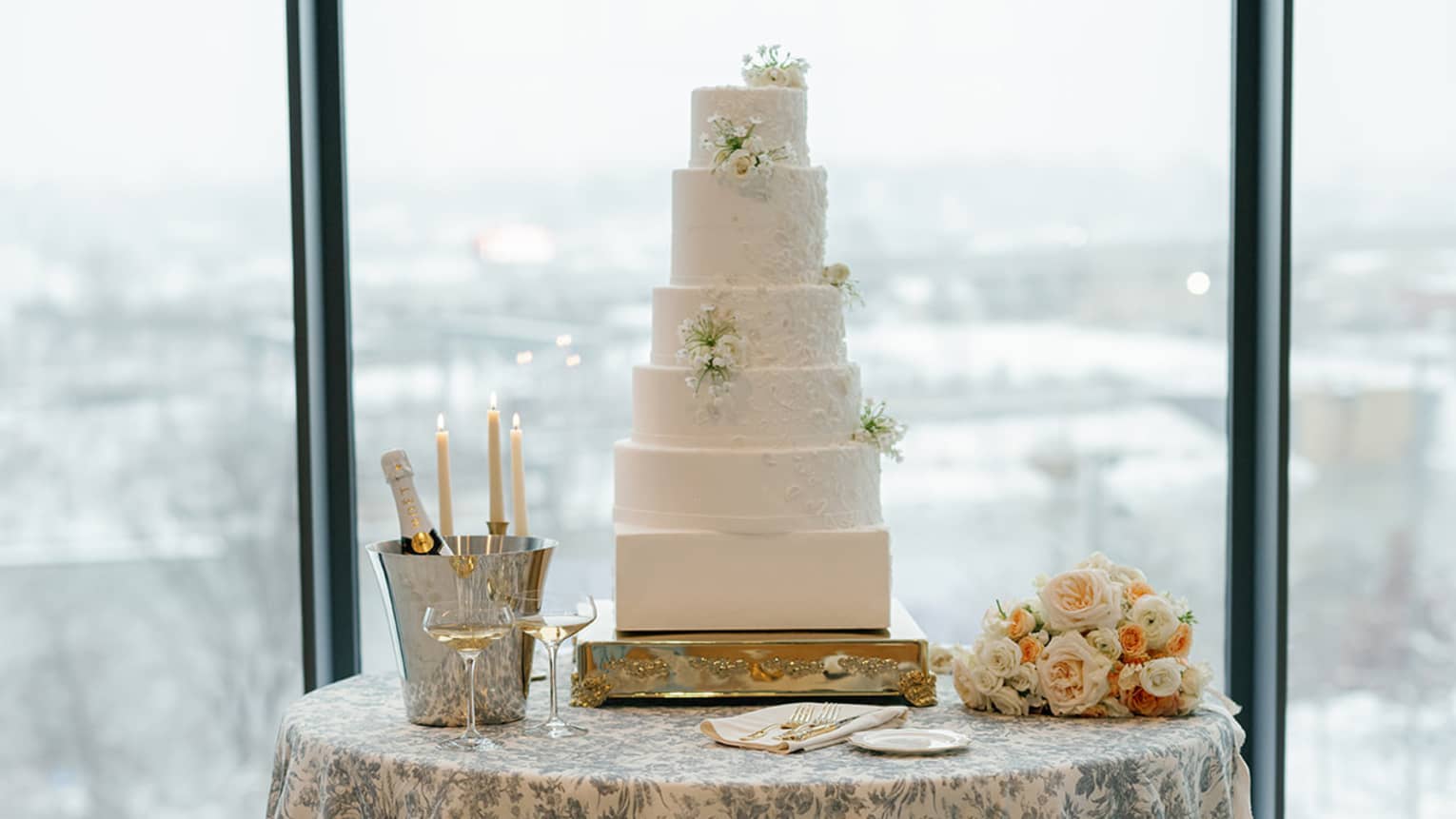 Five-layer wedding cake on top of table with a blue floral tablecloth.