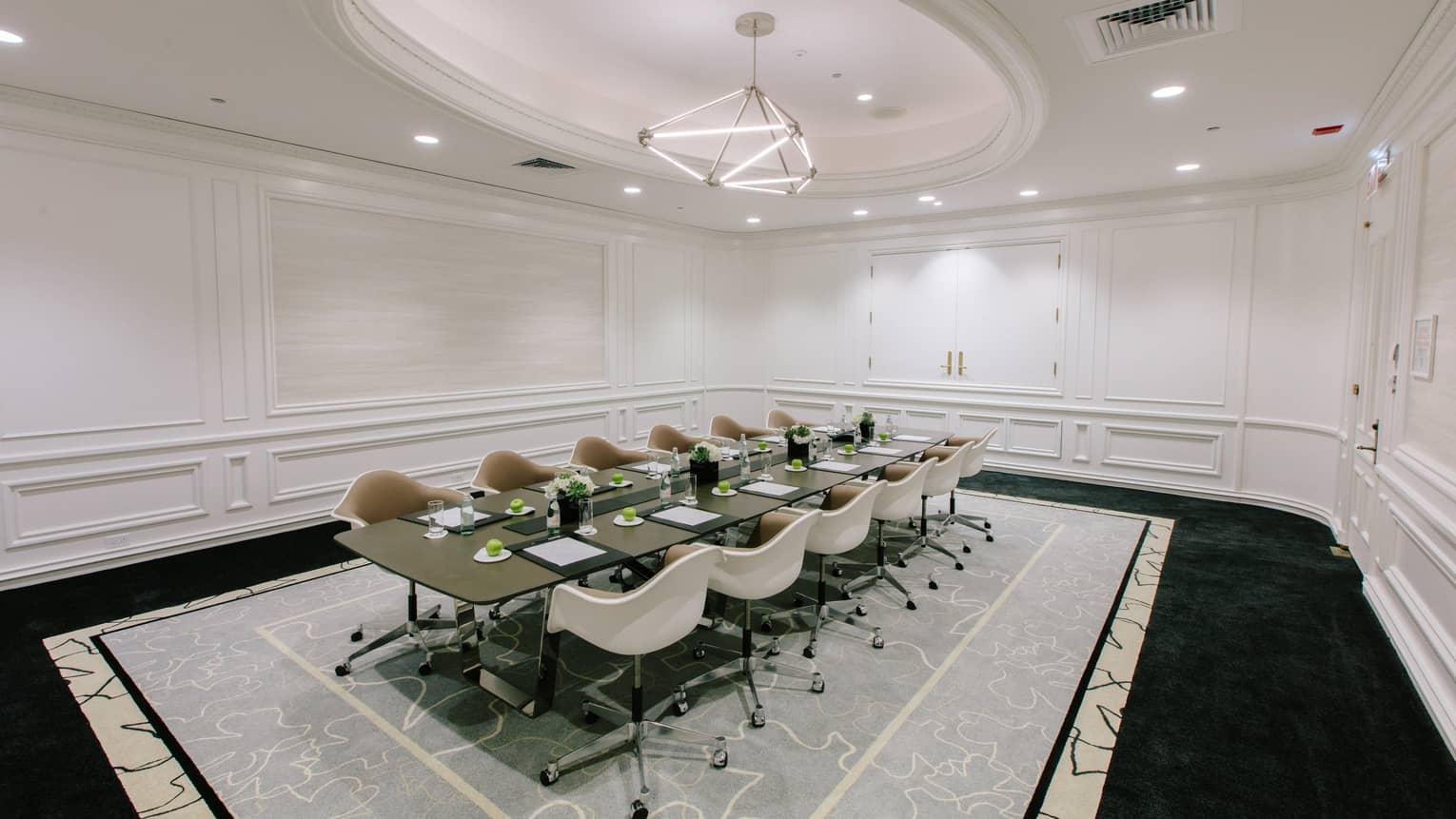 A large meeting room with a long table and white chairs.