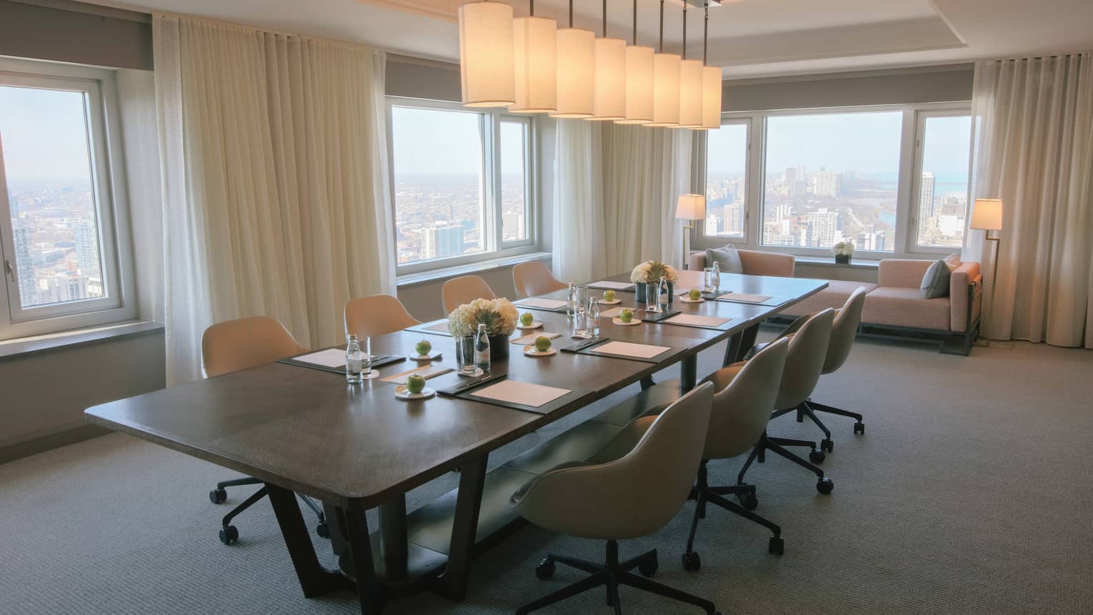 A meeting room with dim lights and a large wooden table with large windows around the room.