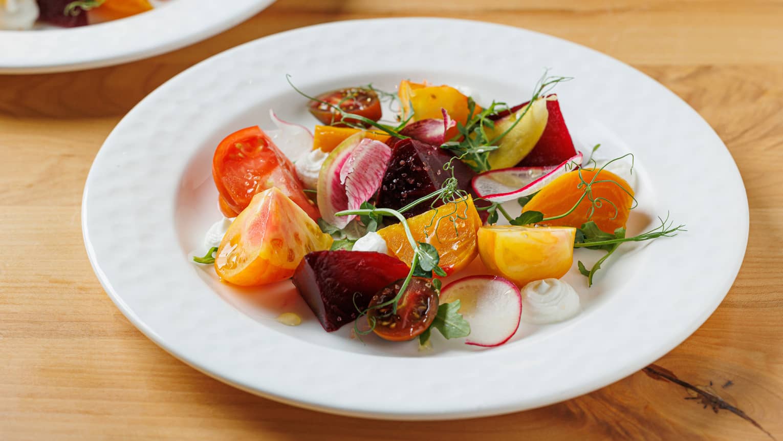 Roasted multicolour beets with shaved radish and fennel greens on white plate