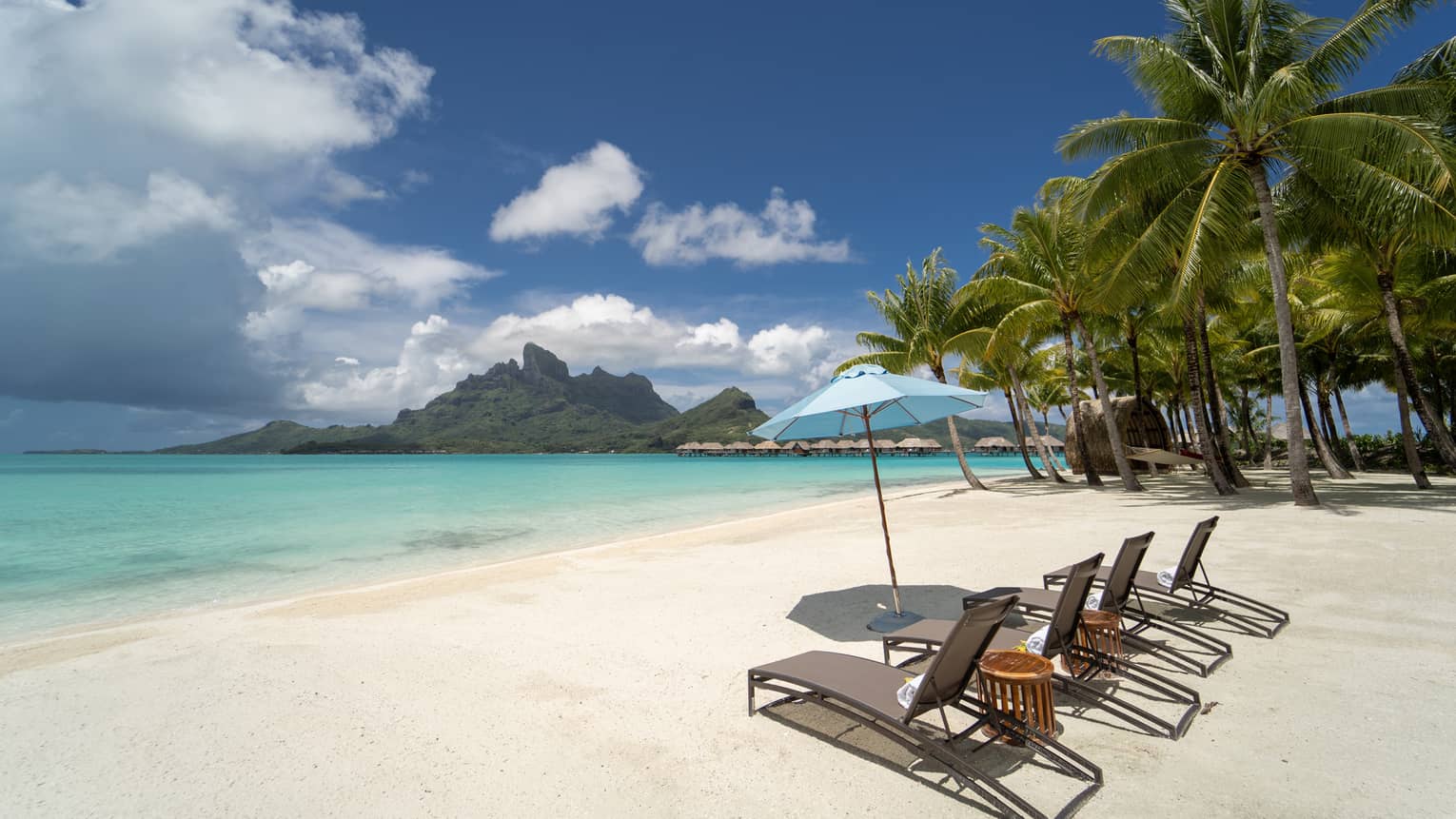 White-sand beach in Bora Bora with four lounge chairs and umbrella