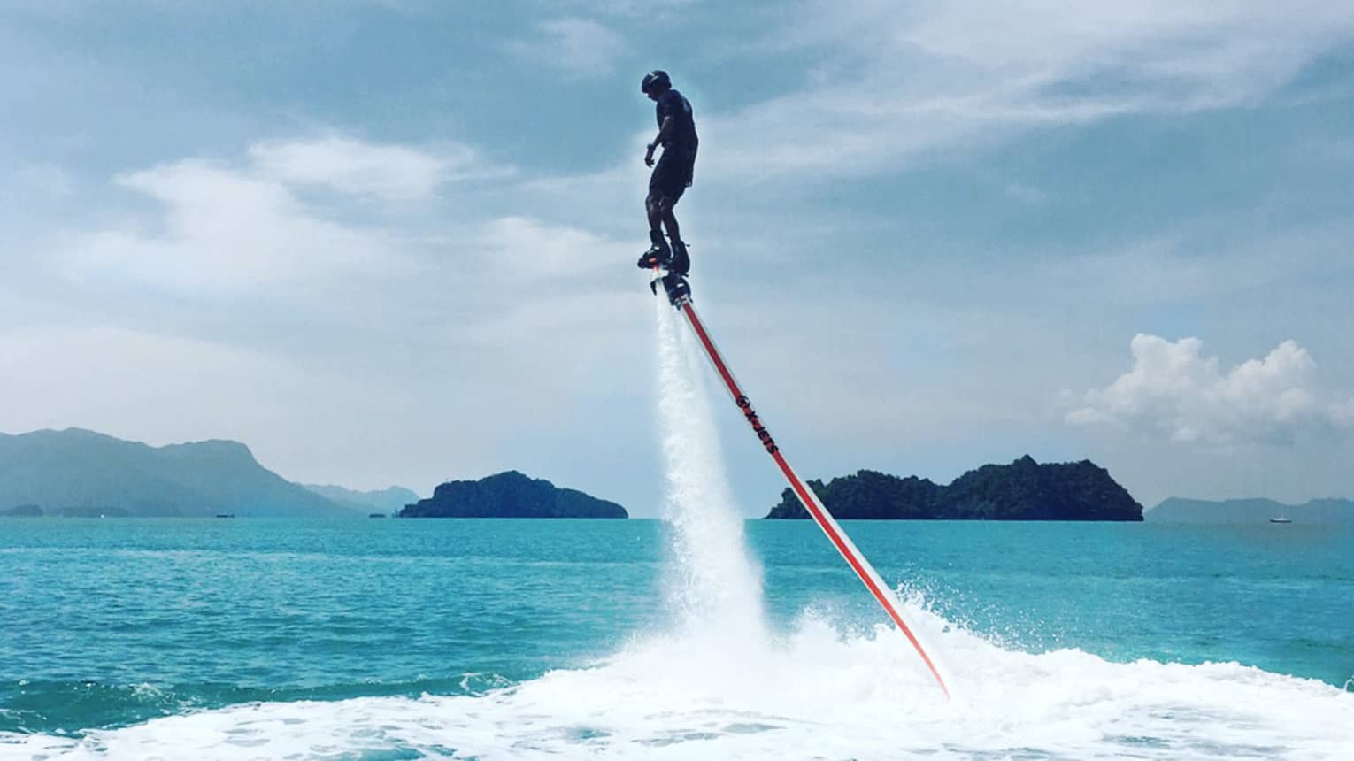 Water sprays as man soars above ocean attached to line, jet blade pack