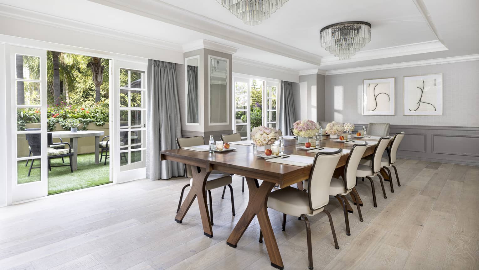 A meeting room with long wooden table, beige chairs and open patio doors.