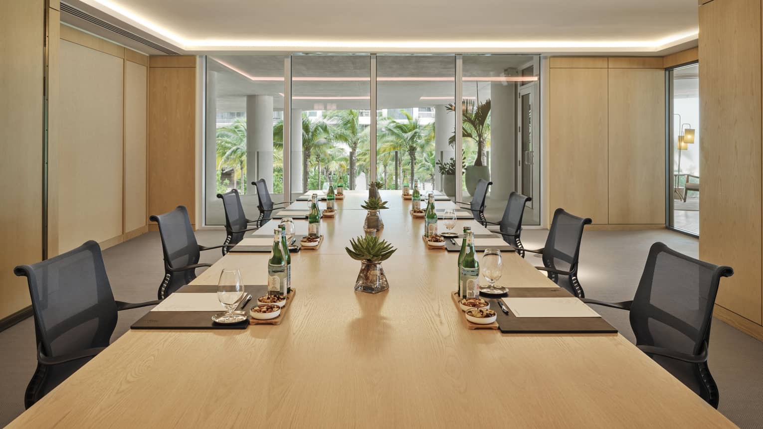 A meeting room with a long wooden table, black chairs and a large window.