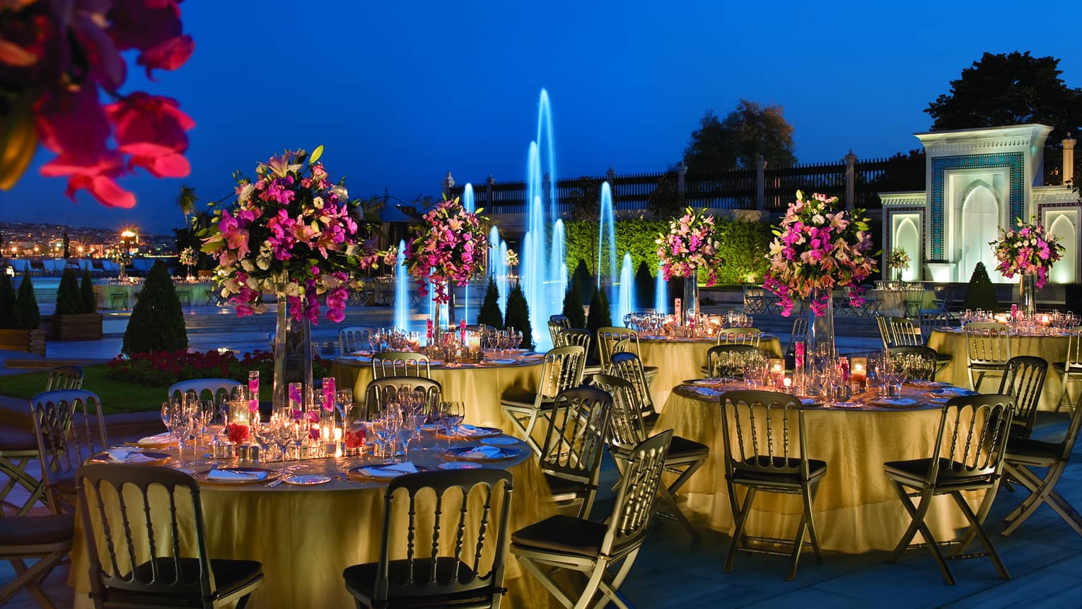 Wedding reception banquet tables with flowers at night in front of fountain with blue lights 