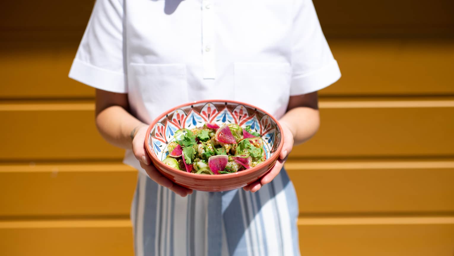 Person holding a Mexican-inspired serving dish with a fresh salad in it