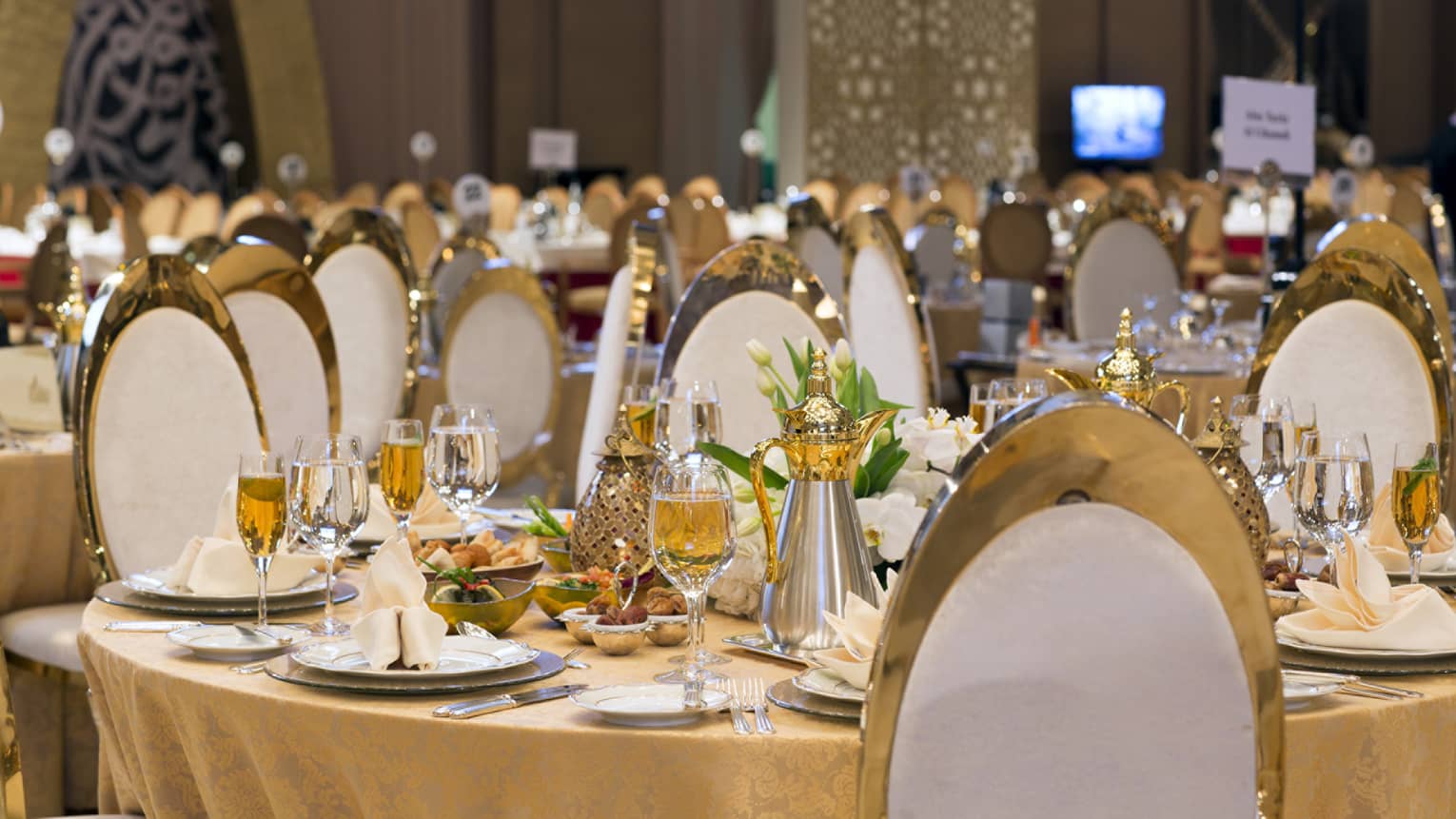 Round table set for dinner with wine glasses, flowers, napkins and white and gold chairs