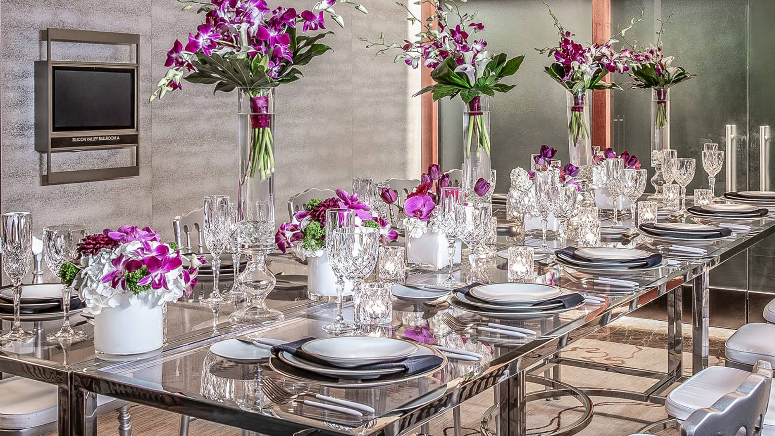 Purple flowers, goblets and place-settings decorate a glass able in an event space
