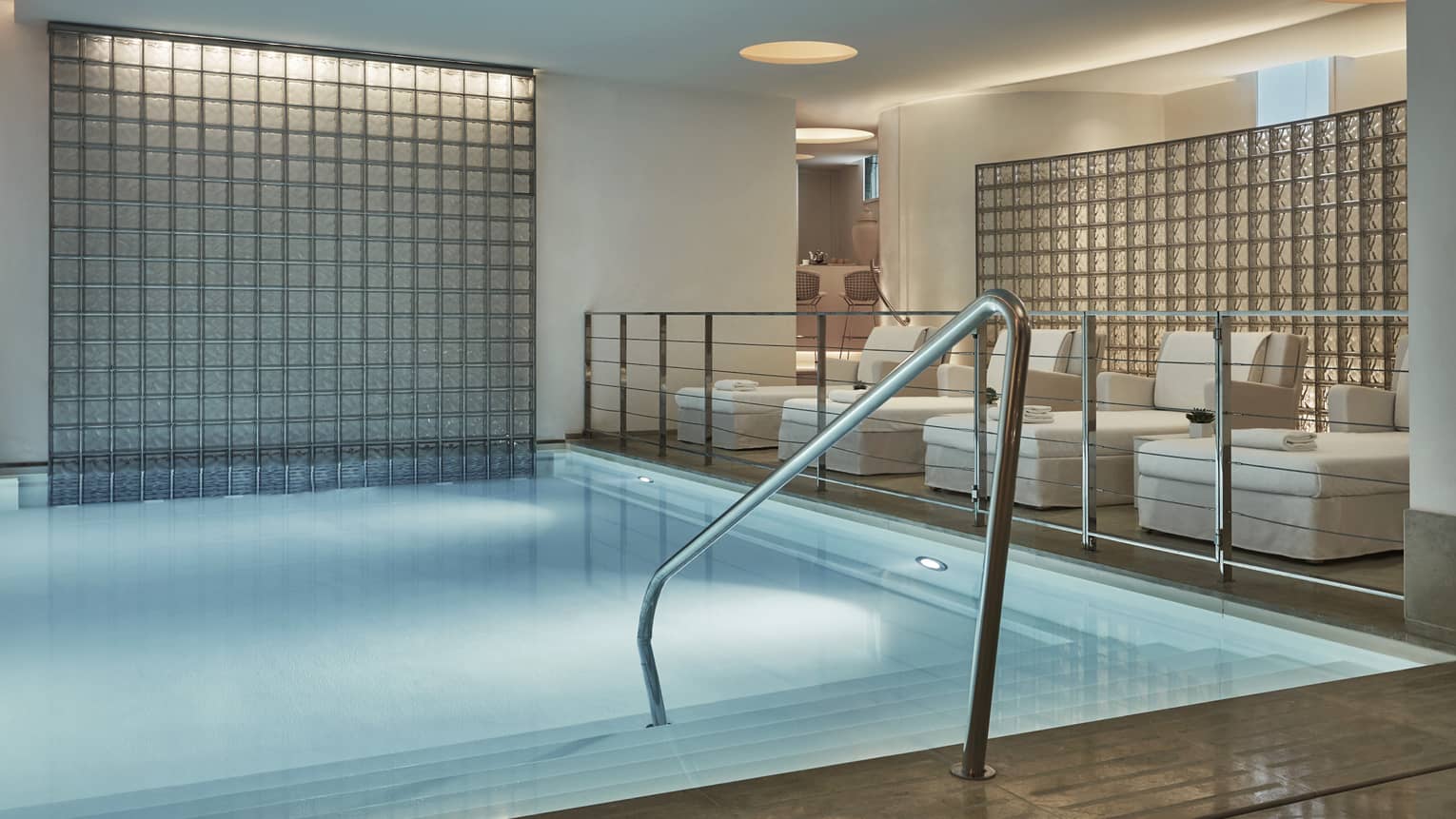 Railing into indoor spa pool under platform with white lounge chairs