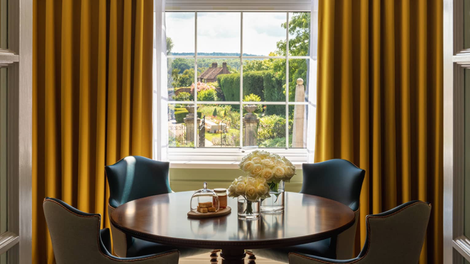 Small round table with four leather chairs, window with yellow drapes overlooking the garden