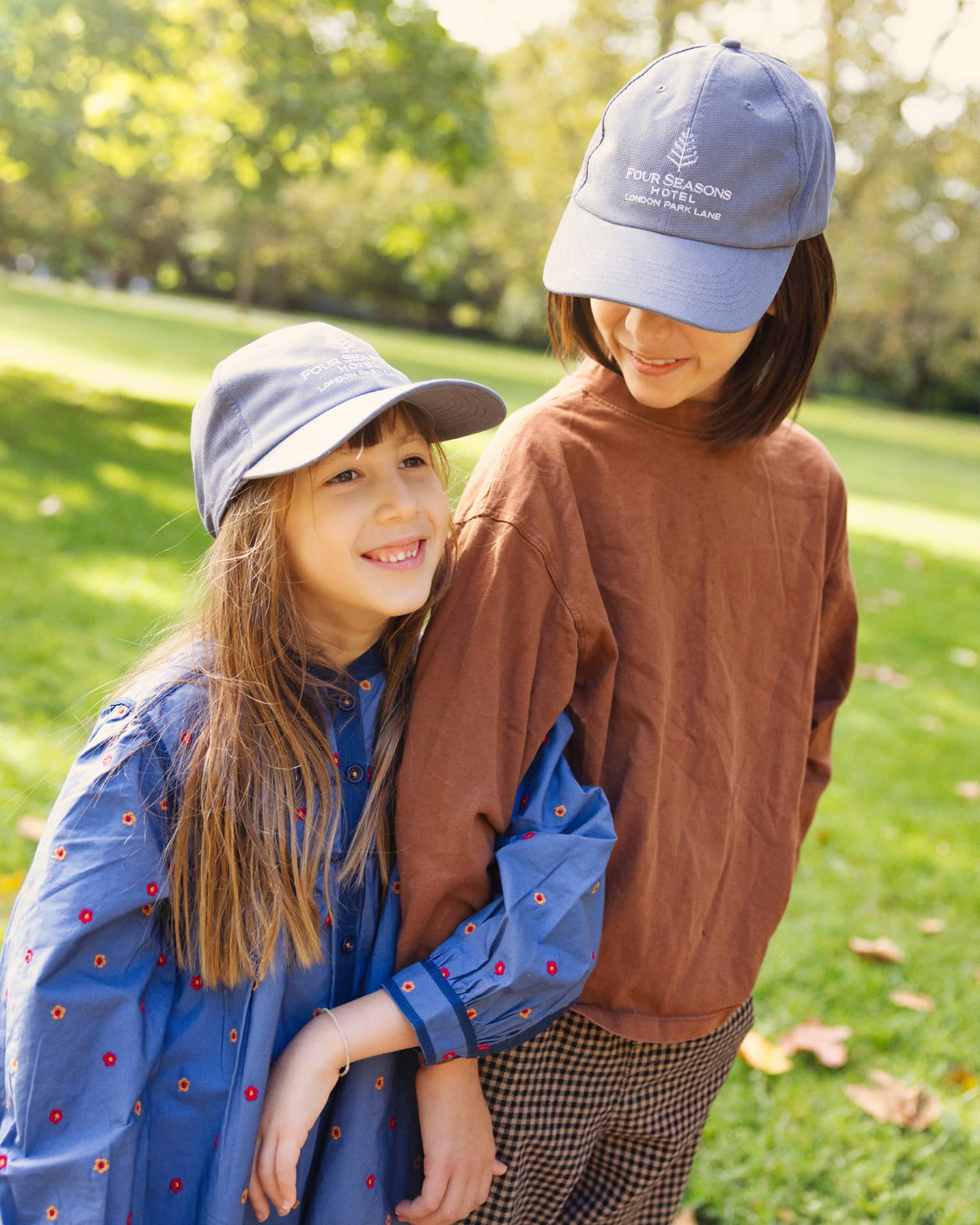 Two girls outside in fall clothing wearing blue Four Seasons Hotel baseball caps