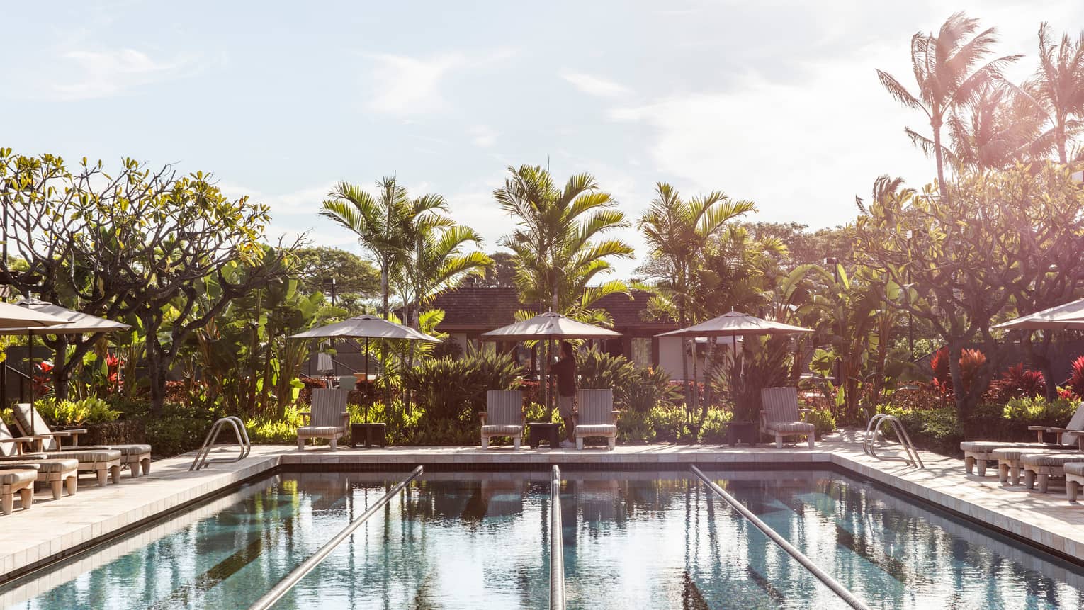 Lap pool at Four Seasons Resort Hualalai with lounge chairs in the shade of umbrellas and palm trees in the wind