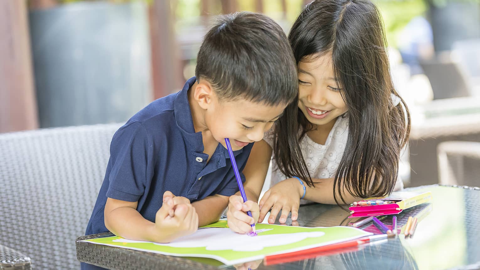 Smiling young boy and girl colouring in book with crayon
