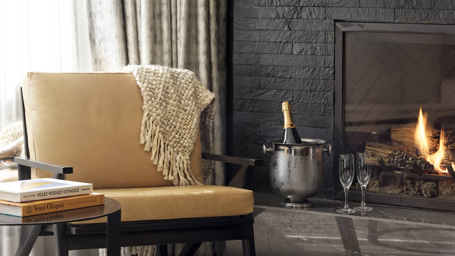 Leather chair, round side table, fireplace, ice bucket with bottle of champagne and two flutes