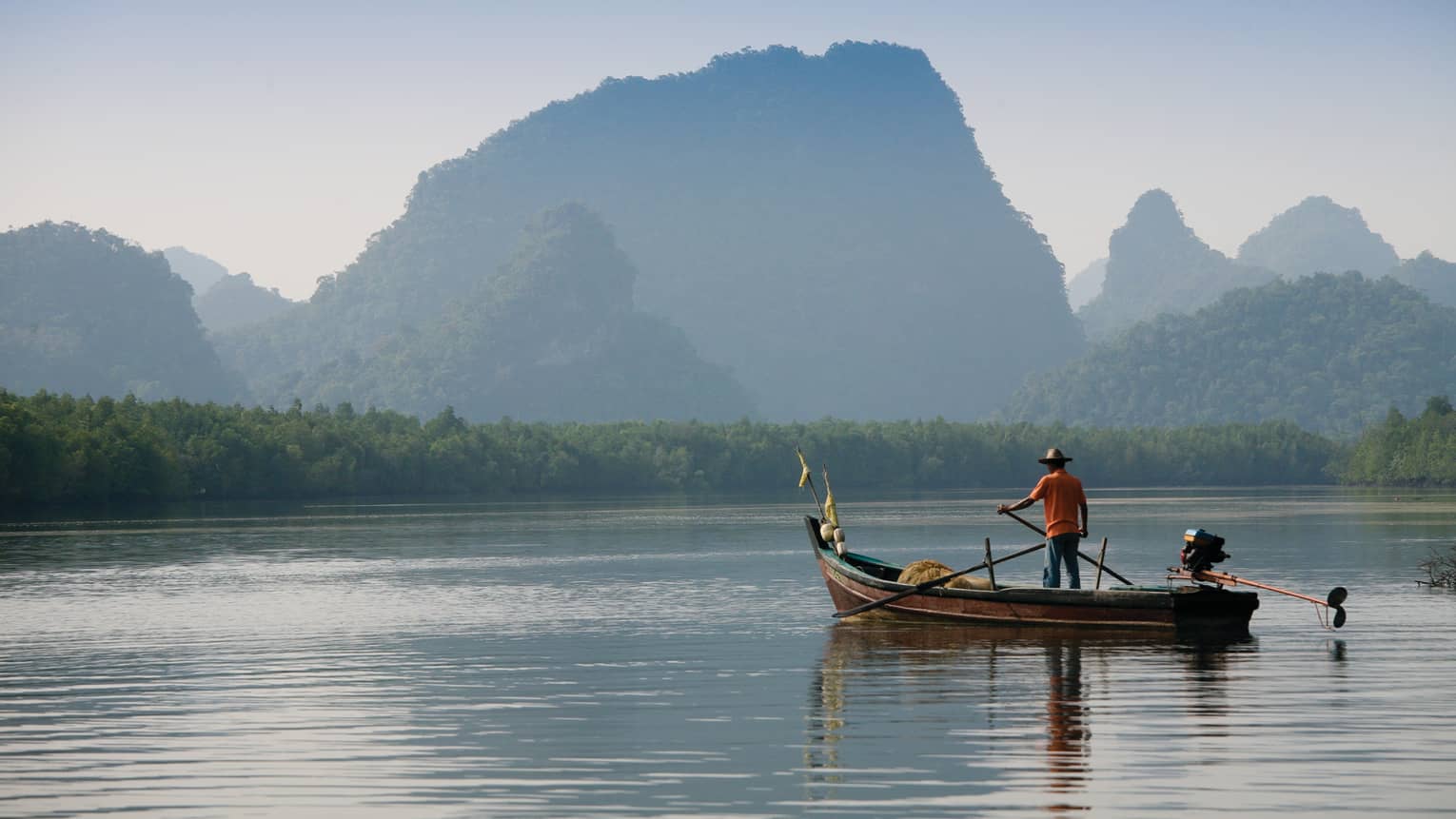 Man in a boat on Langkawi river with mountains in the background