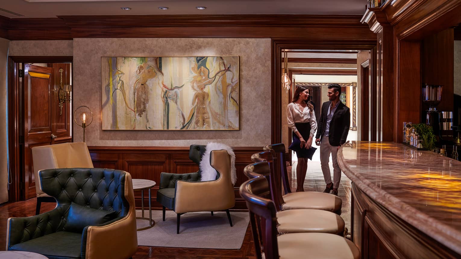 Woman and man walk through door into cocktail lounge with large painting, leather chairs
