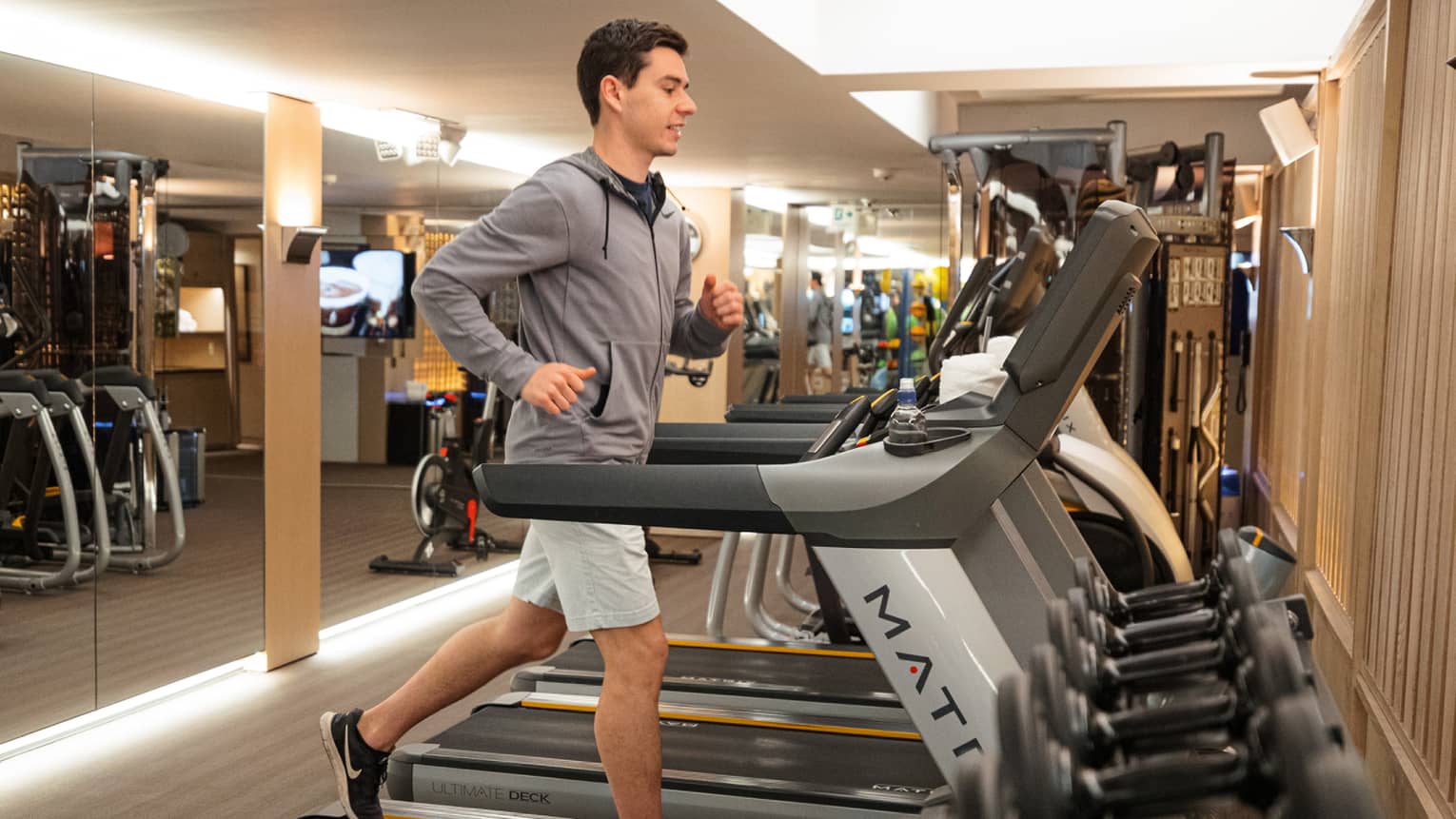Man wearing grey shorts and a hoodie running on a treadmill