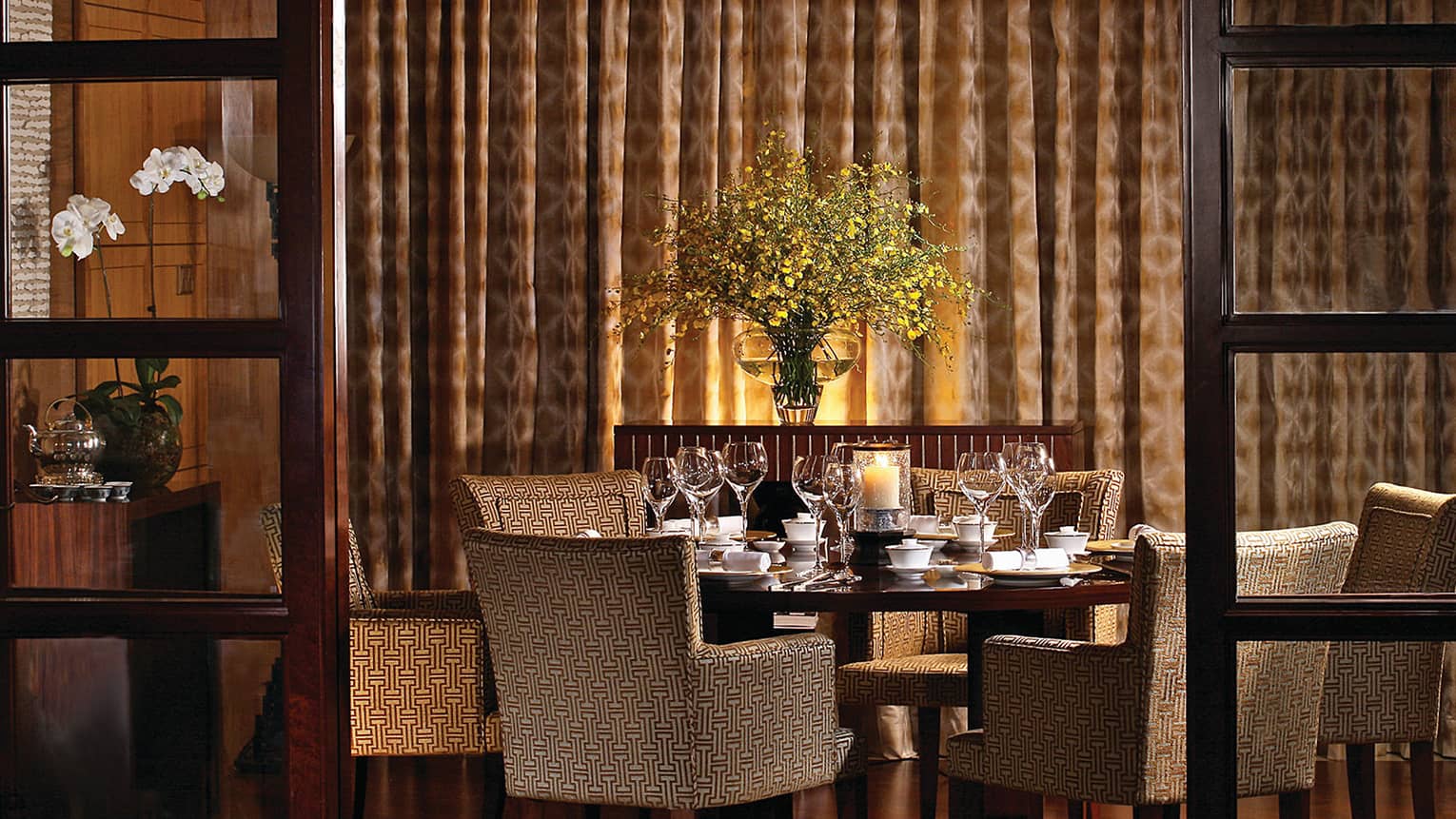 Upholstered dining chairs around wood table in dimly-lit dining area by wall, curtains