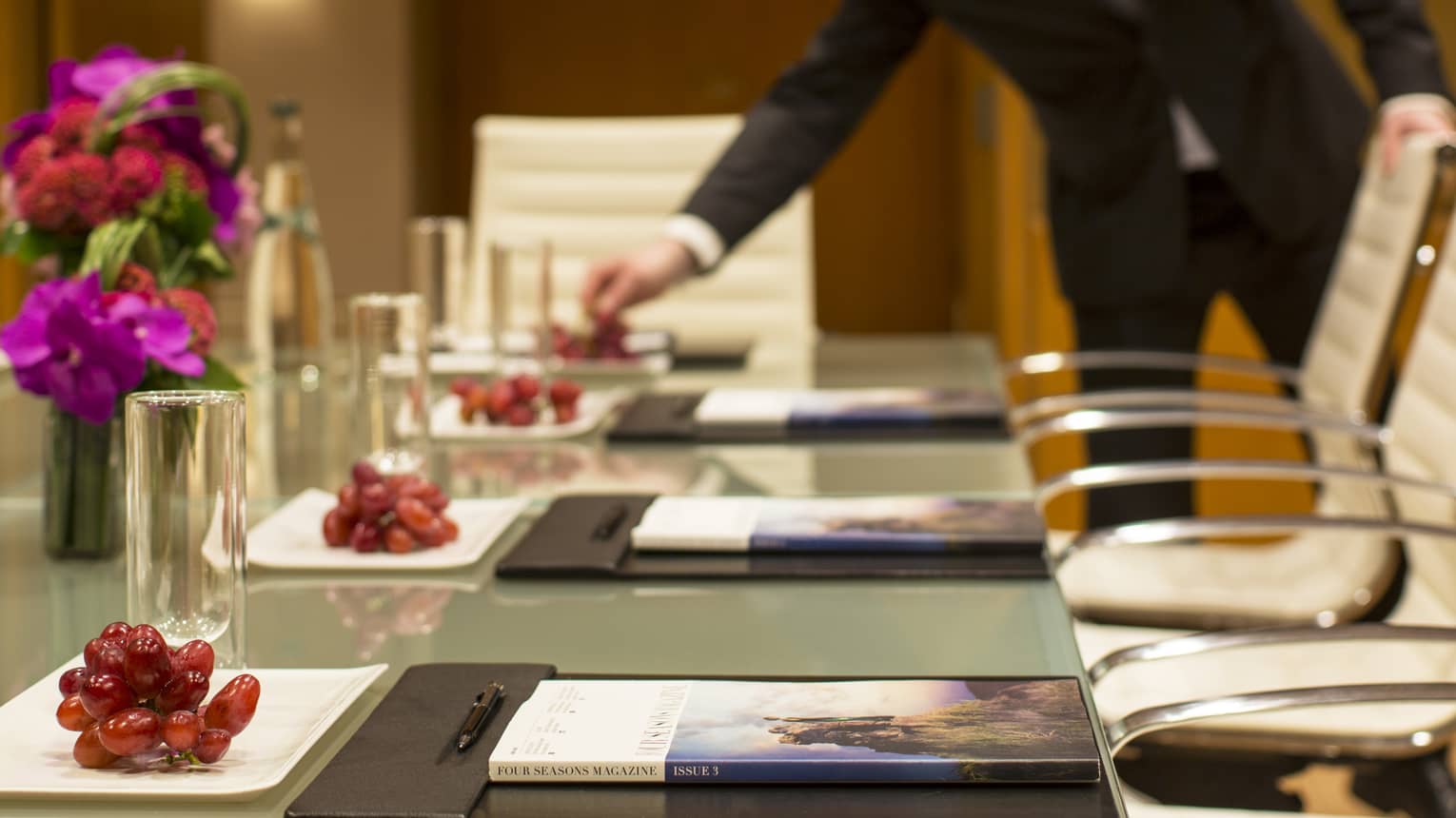 Boardroom meeting table, man wearing suit reaches for red grapes on plate