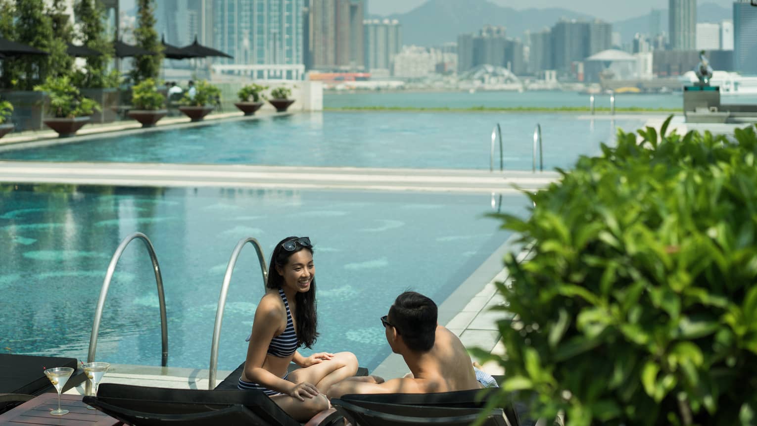 Couple wearing swimsuits on outdoor swimming pool deck, city skyline in background