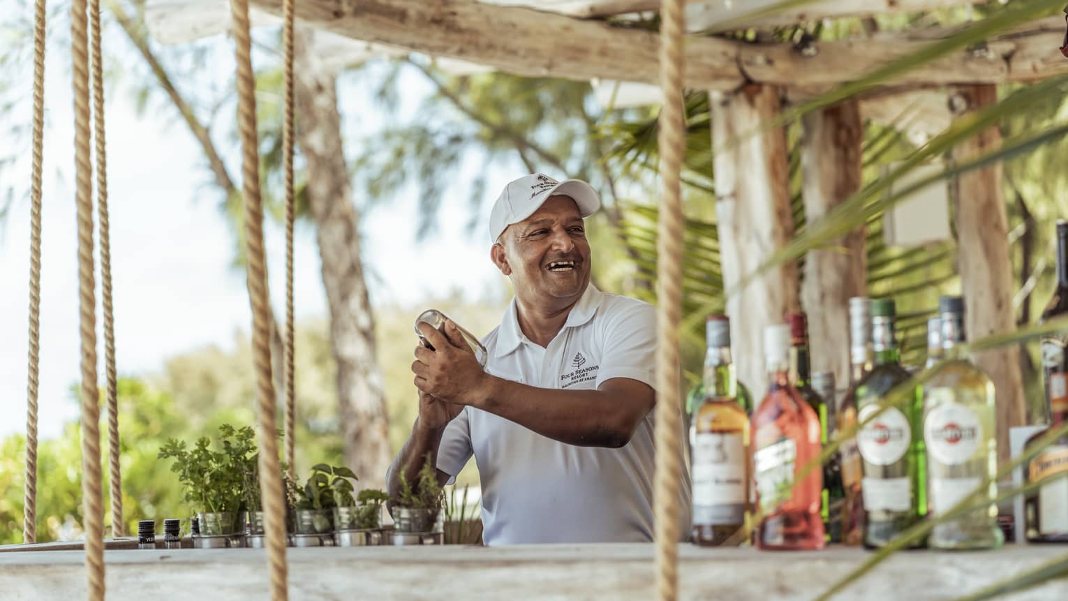 A smiling bartender in a ball cap shakes up a cocktail