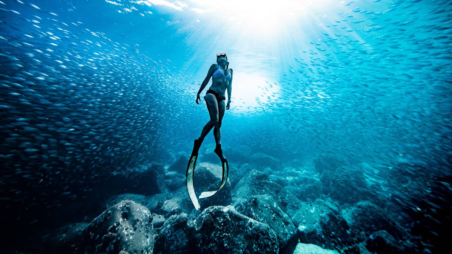 A woman in bikini wears scuba slippers below the surface of the ocean water