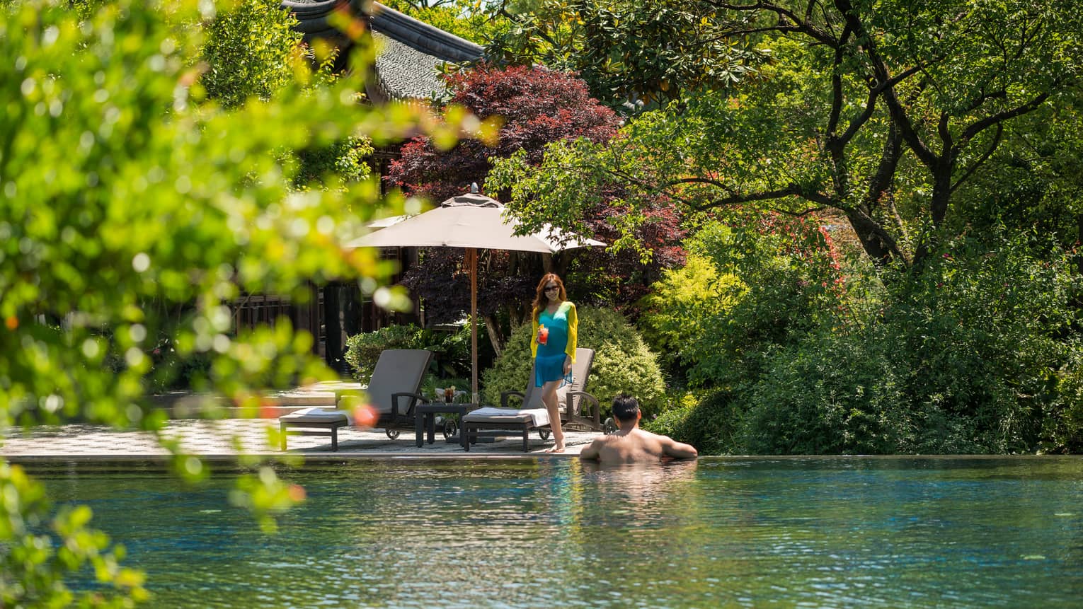 Woman in blue dress walks towards man wading in outdoor swimming pool
