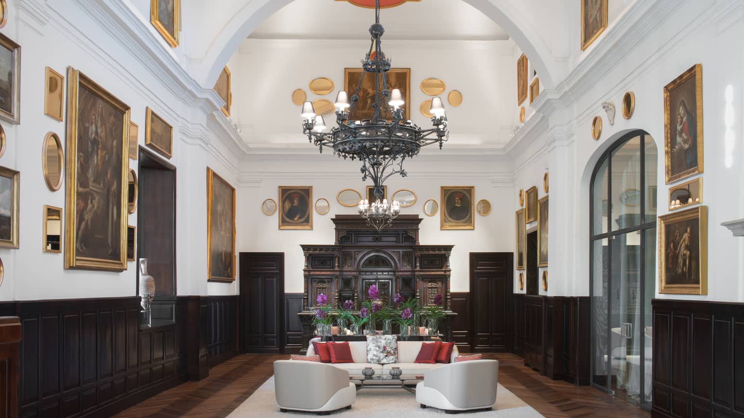 Sala Museo with artwork lining both walls, white leather furniture, high ceilings, wrought iron chandelier, fireplace