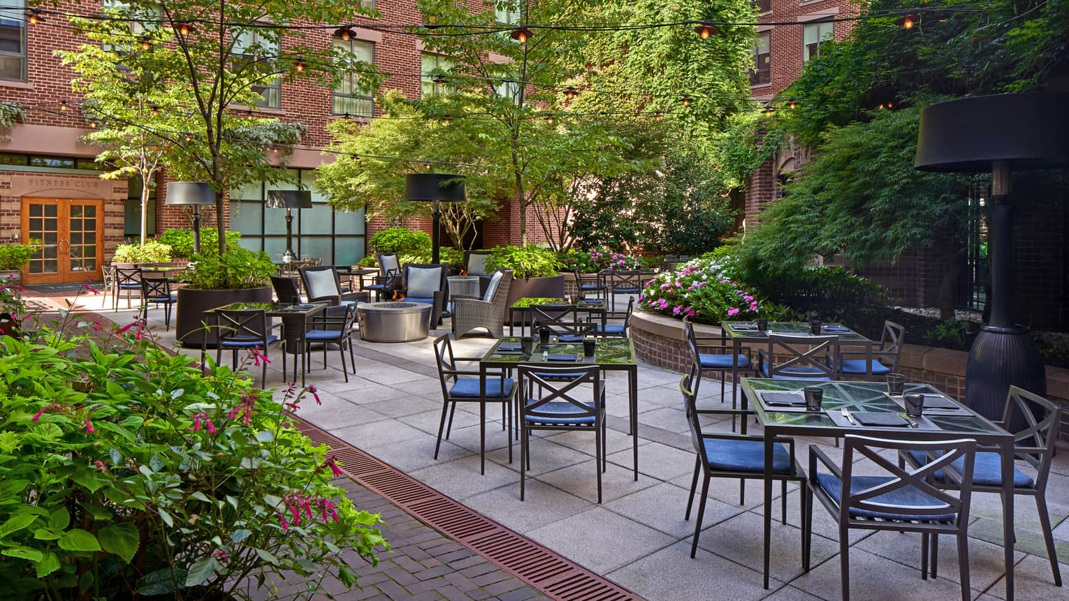 An outdoor eating area with metal chairs and glass tables surrounded by plants.
