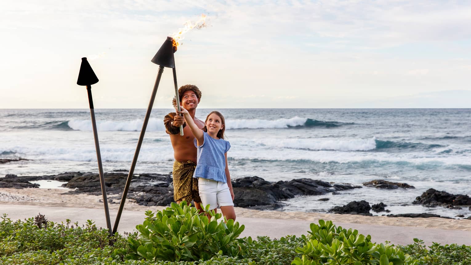 A father and daughter lighting lanterns along a beach shore together.