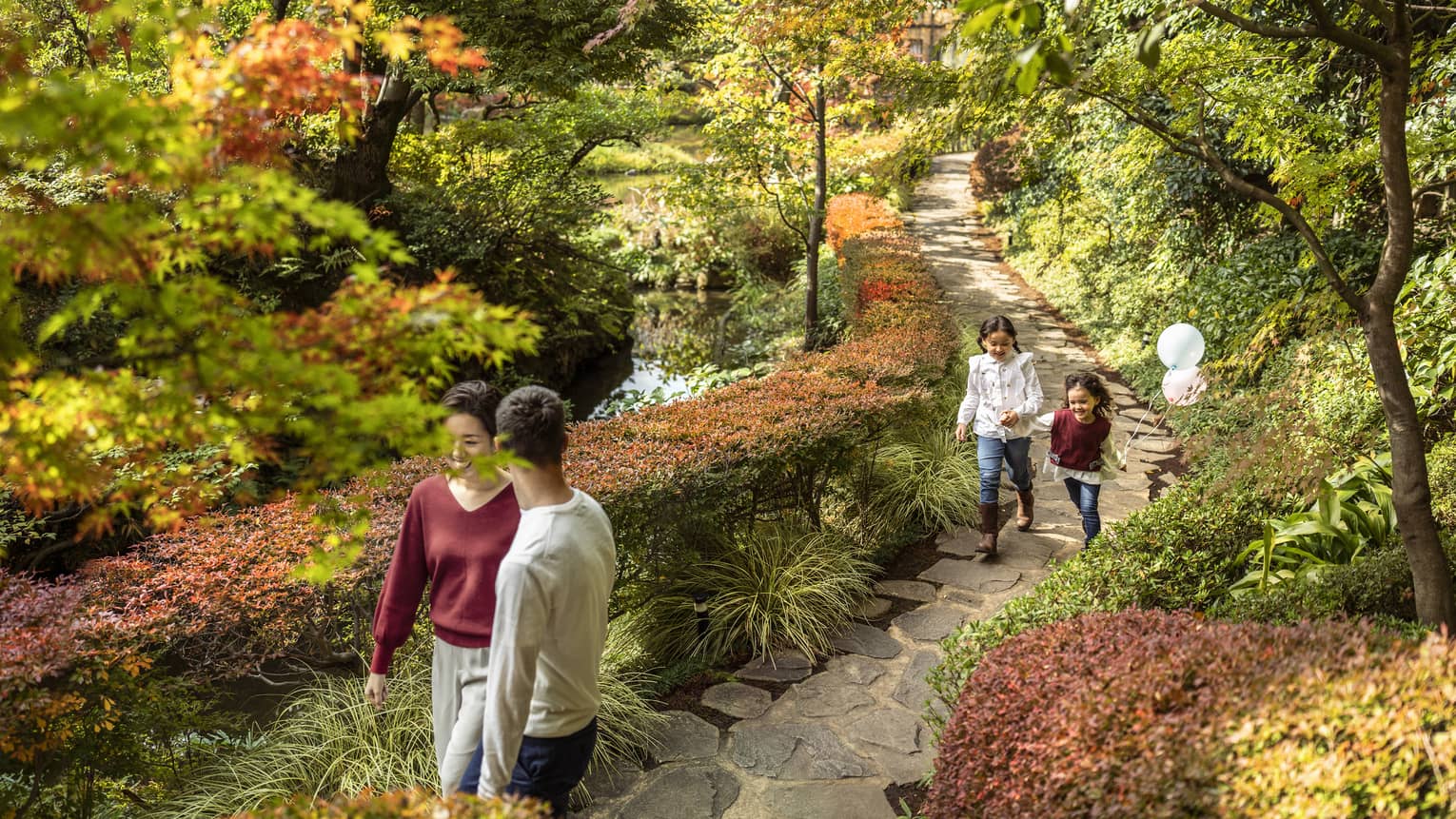 Couple and their two daughters walk along foliage-lined pathway parallel to the koi pond