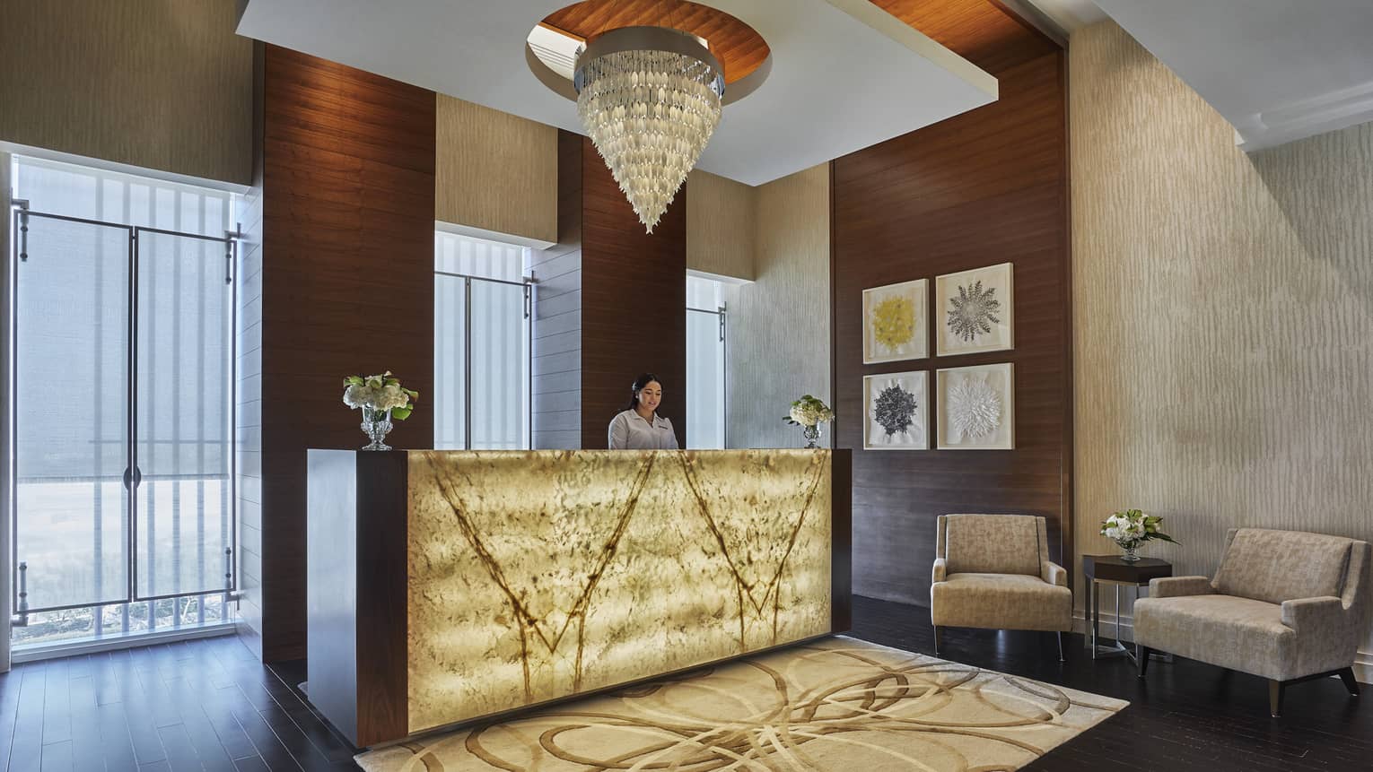 A yellow glass chandelier hangs over the welcome desk, adorned with soft yellow light and a brown rug. 