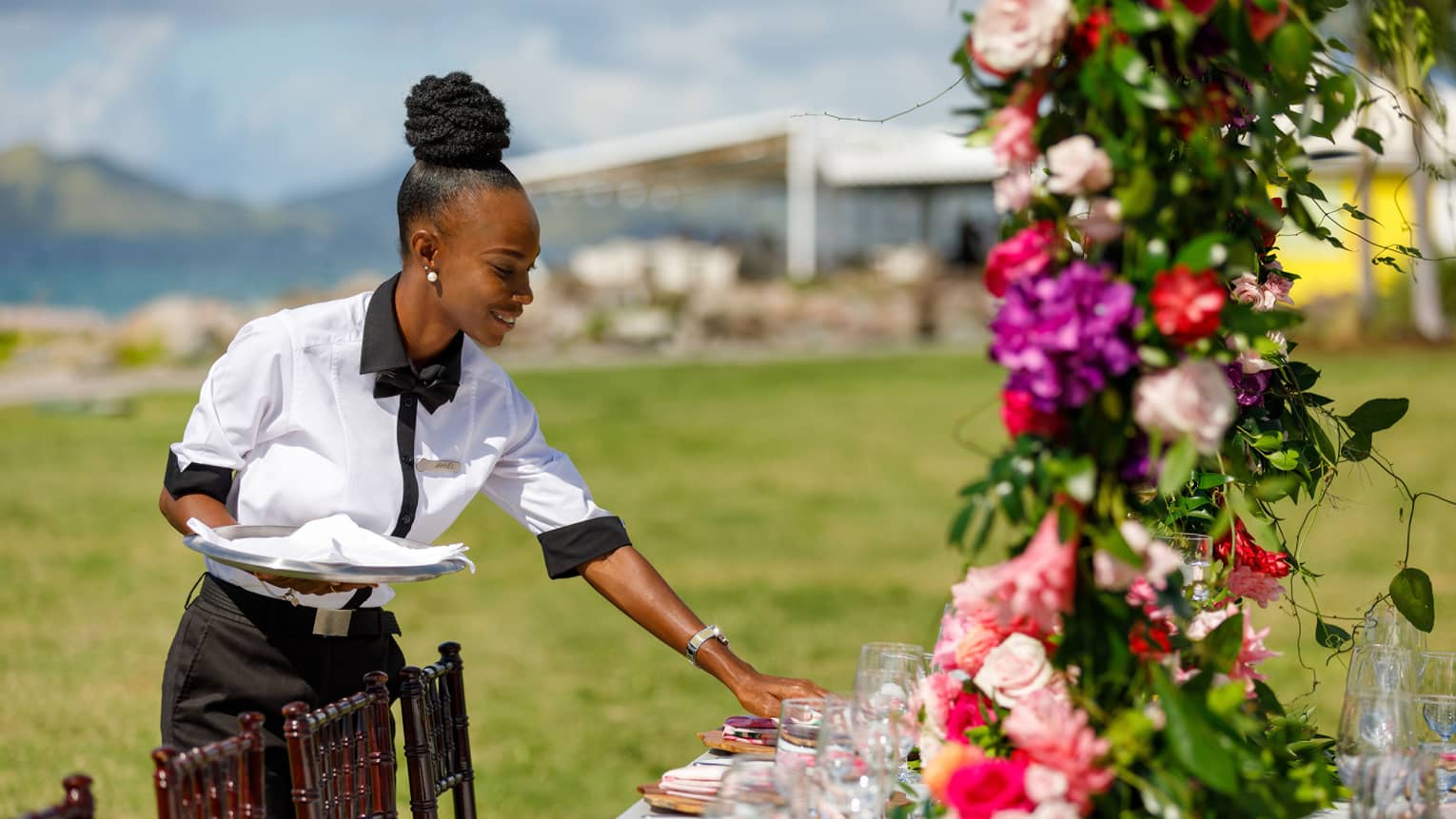 Uniformed wedding service specialist adjusting table setting, pink floral arrangement in forefront