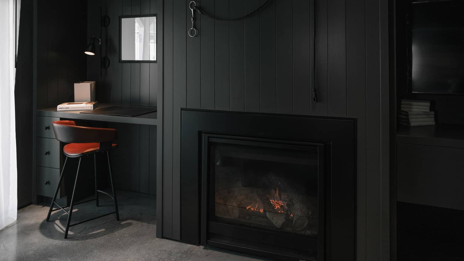 Fireplace in dark-grey wall, next to built-in desk and red/metal chair