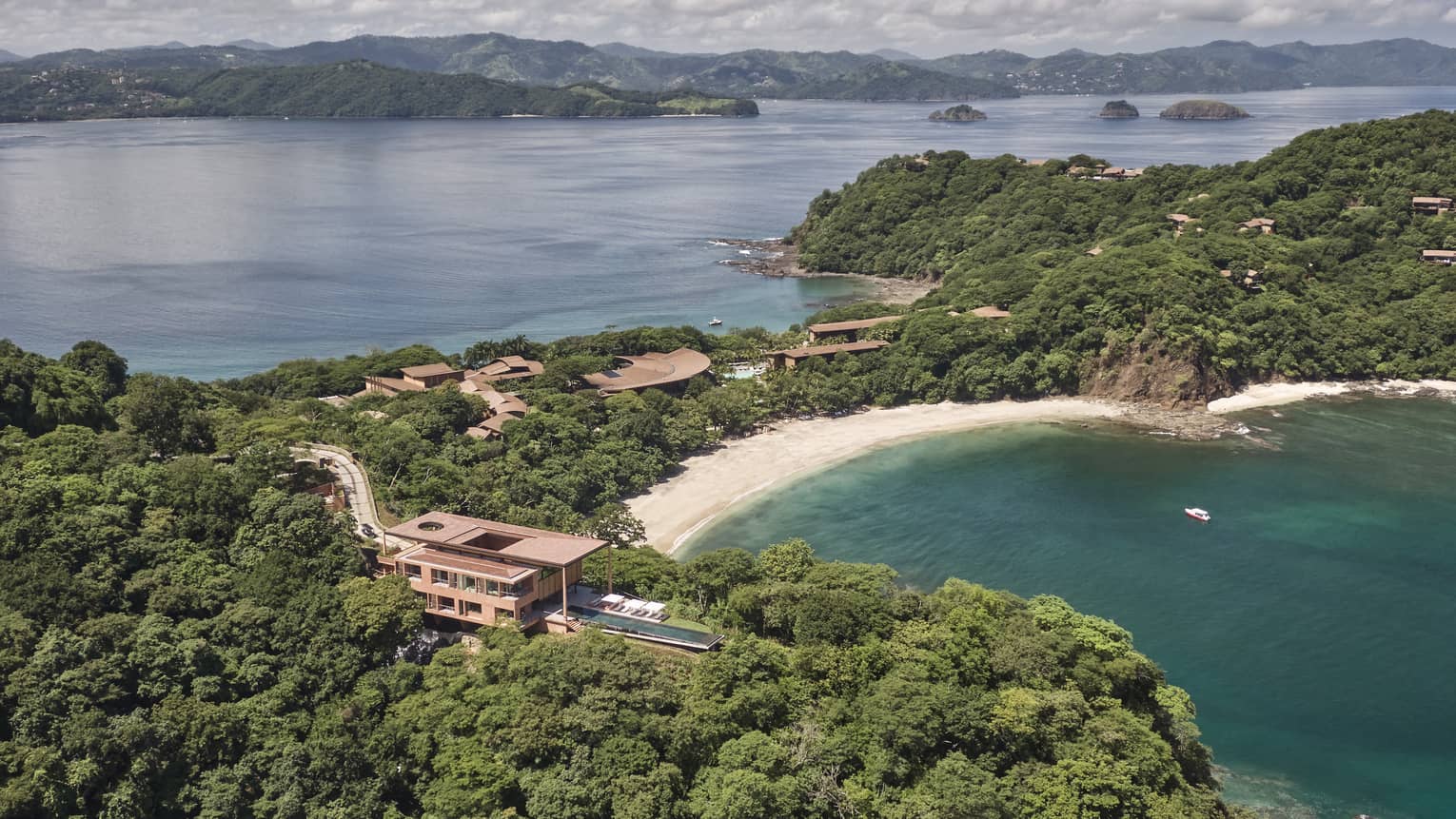 Aerial view of a private villa surrounded by trees near a beach/bay