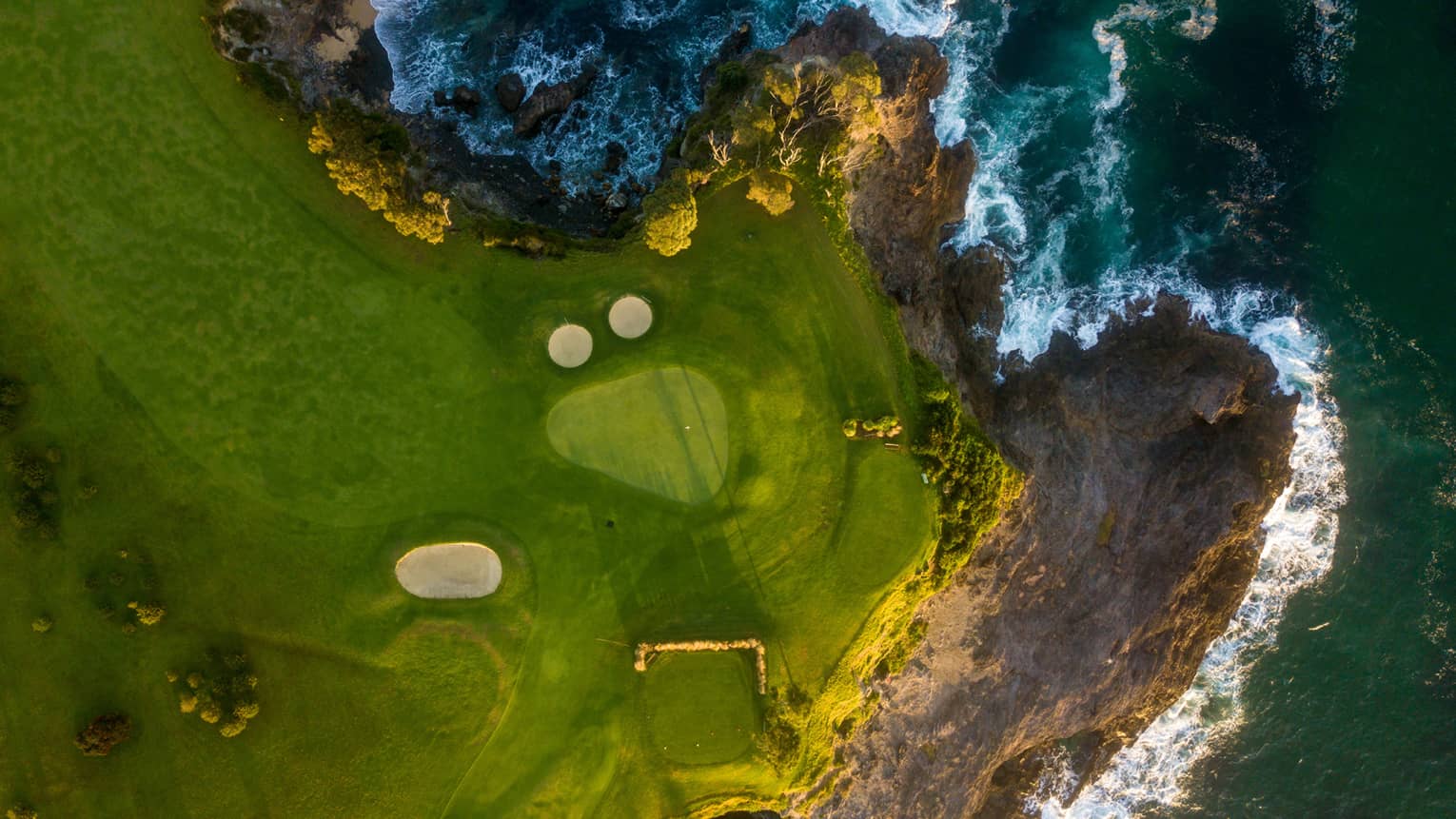 Aerial view of coastal golf course with craggy shores