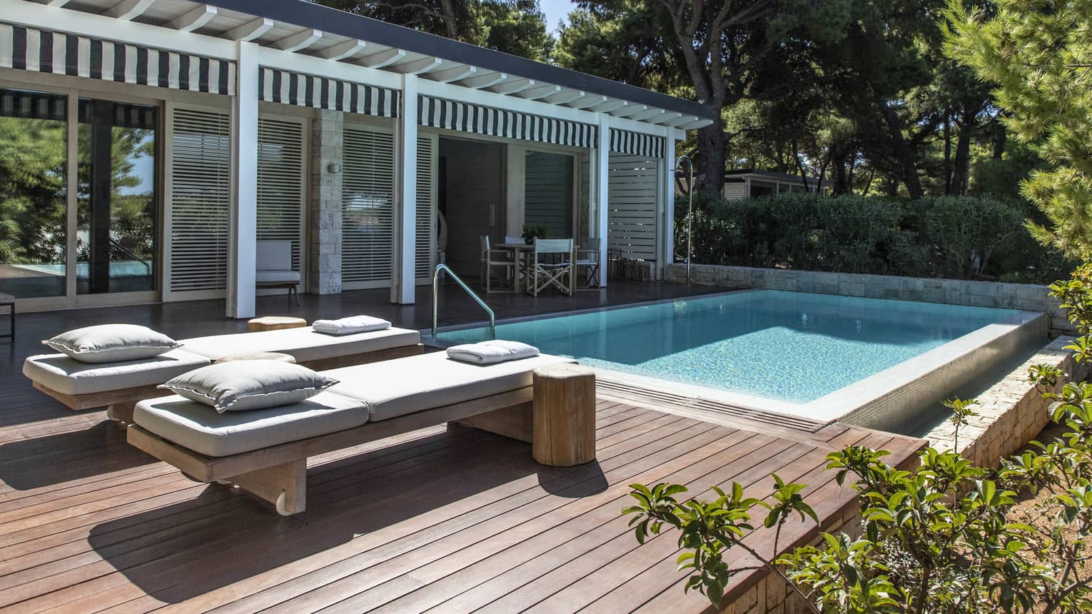 Private wooden deck with two lounge chairs and pool, surrounded by greenery,Private outdoor pool with luxurious sun loungers, contemporary pergola design and lush greenery, offering a private retreat and serene sea views