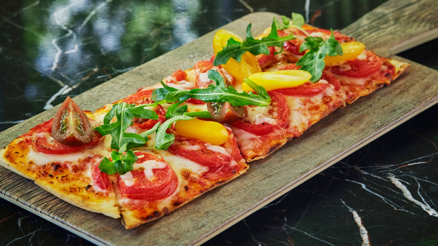 Wood-fired Flatbread pizza topped with tomatoes, fresh greens on wood board
