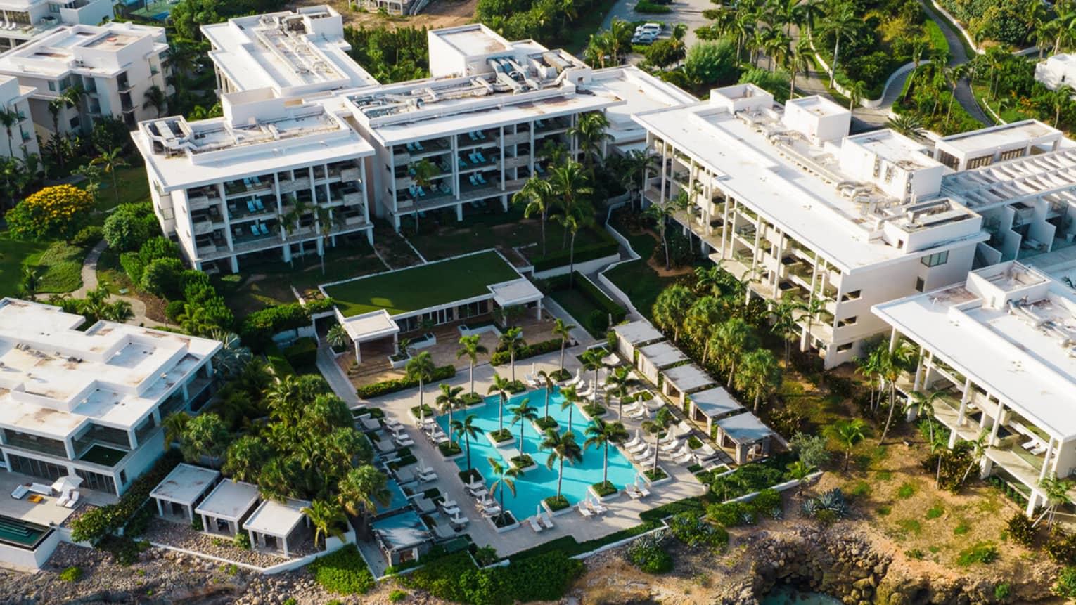 Aerial view of a modern hotel exterior and outdoor pool situated by a turquoise body of water